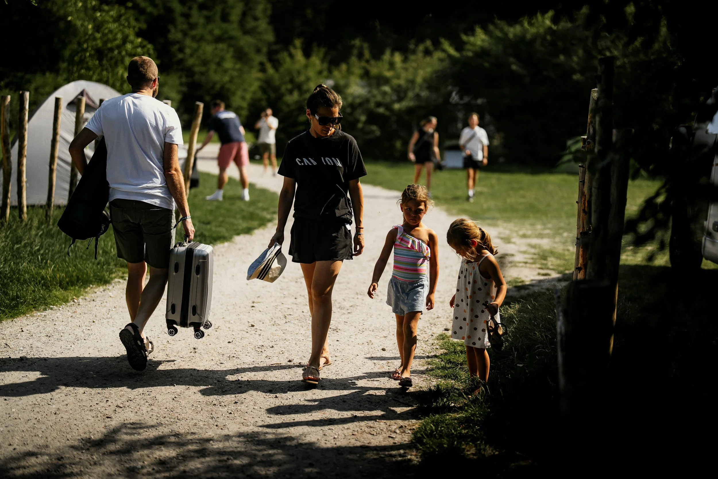 Family walking on a gravel path at a campsite, with children and adults, tents, trees, and other campers in the background. (Graveller)