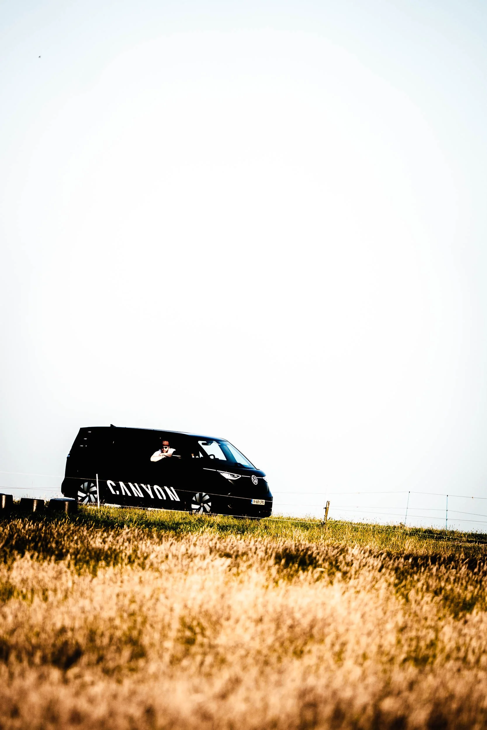 Black van with 'CANYON' logo parked on grassy hill under overexposed sky, person inside taking a selfie. (Graveller) )(Canyon)