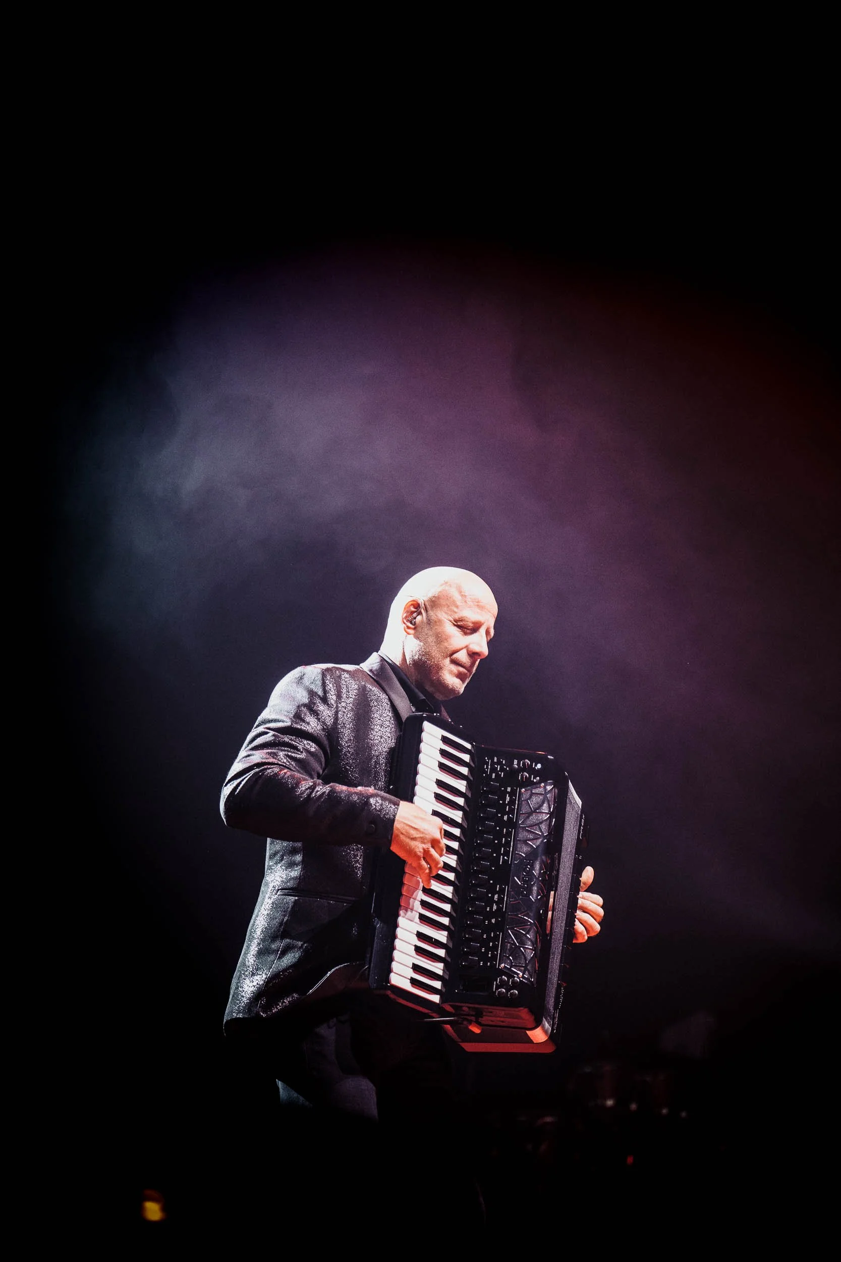 A man playing an accordion on stage with pink and purple lighting.