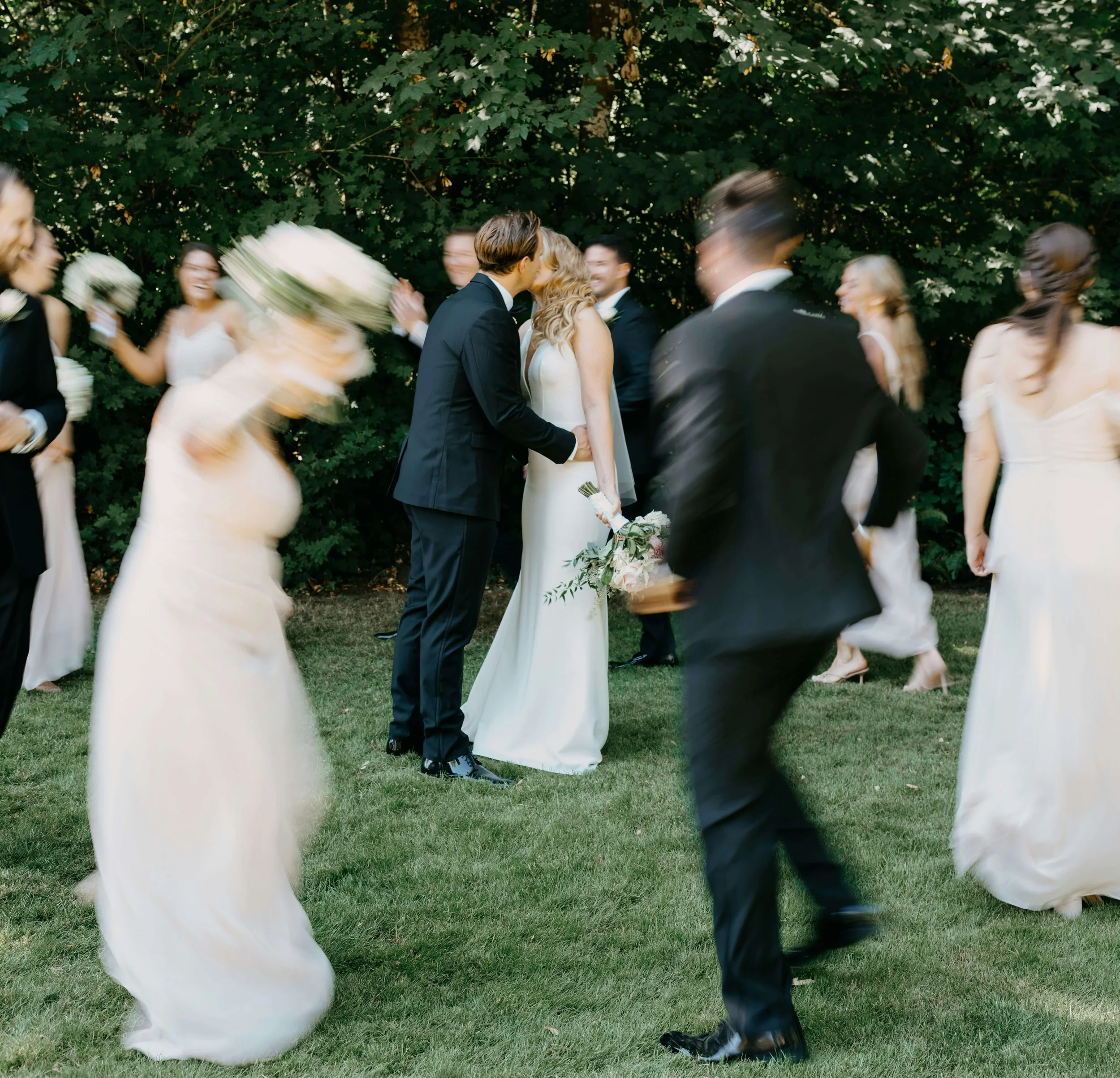 couple kiss during an outdoor wedding ceremony with guests dancing around them
