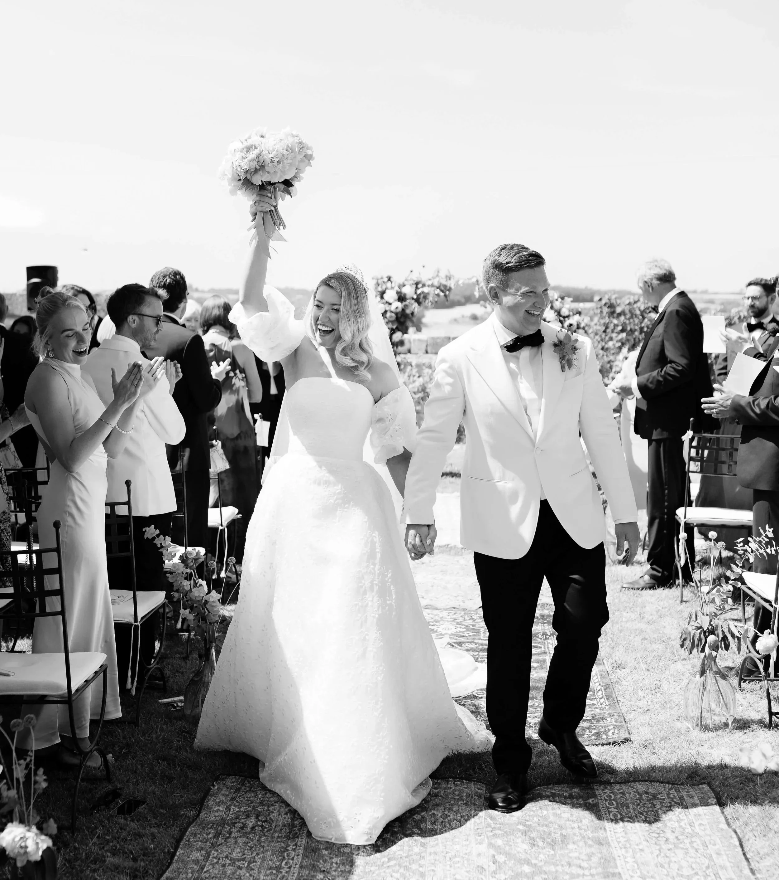 A black and white image of a couple's outdoor wedding with them walking down the aisle