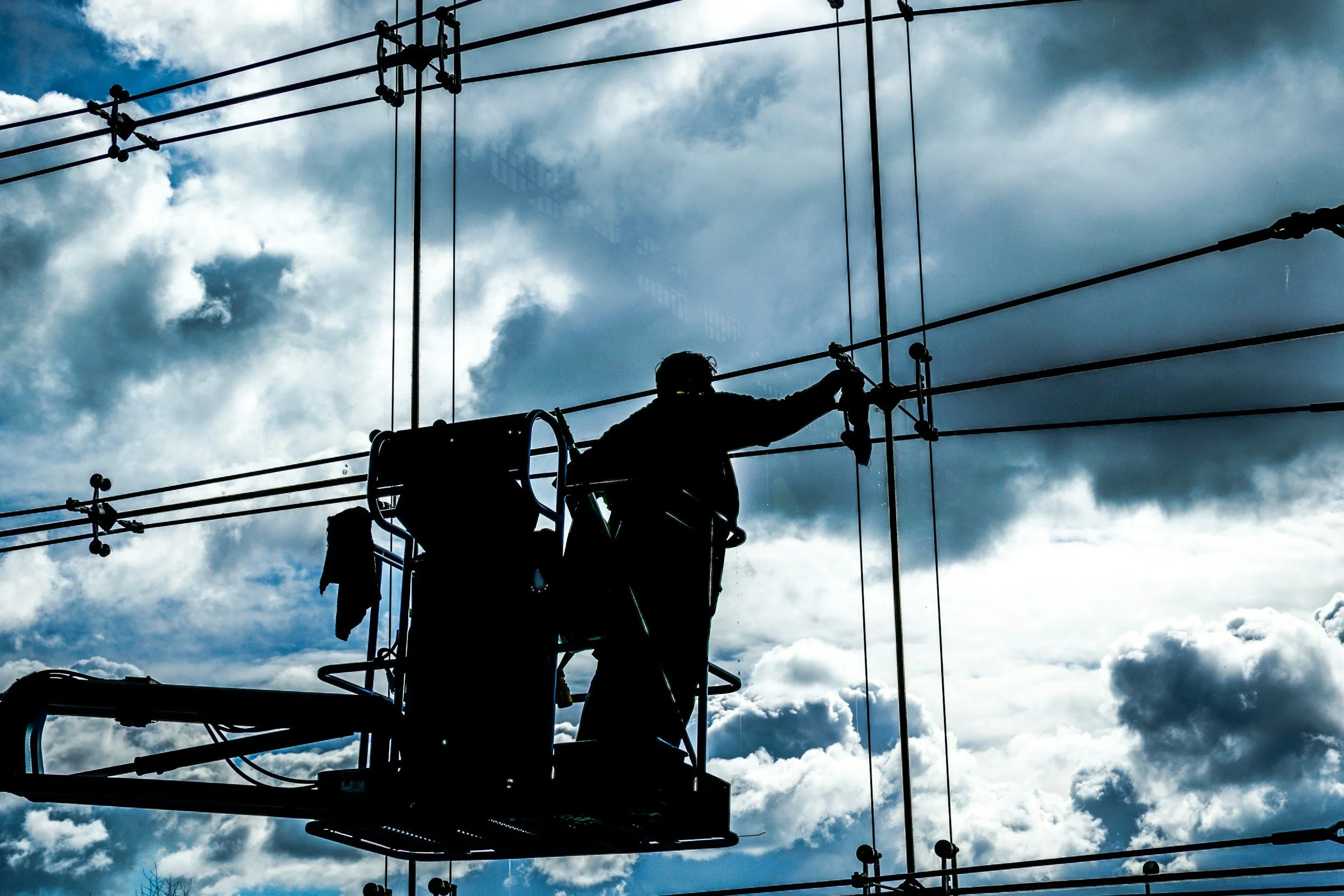 Silhouetted workers on a lift repairing or maintaining overhead power lines against a cloudy sky.