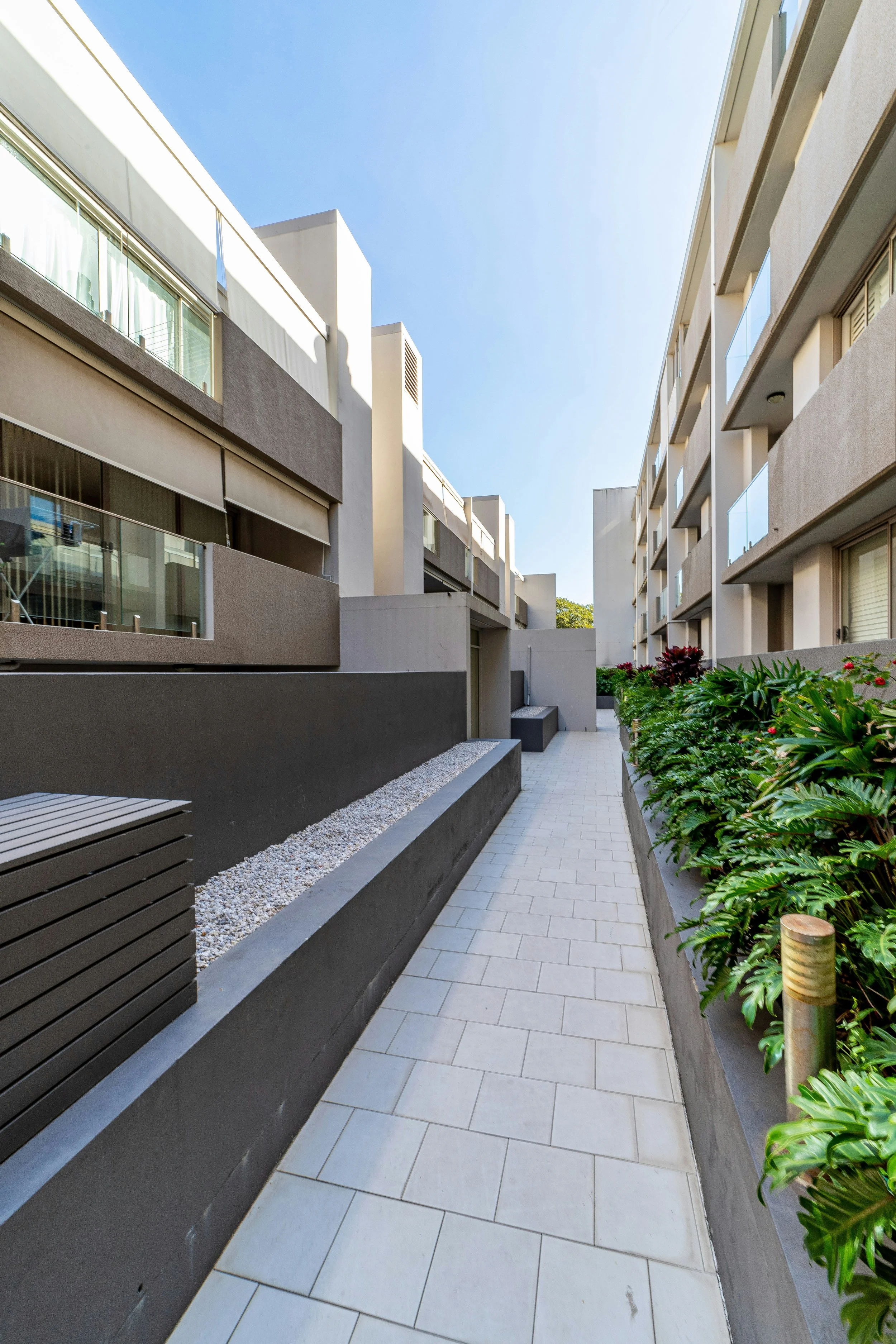 View of a modern apartment complex courtyard with pathways, green plants, and outdoor lighting.