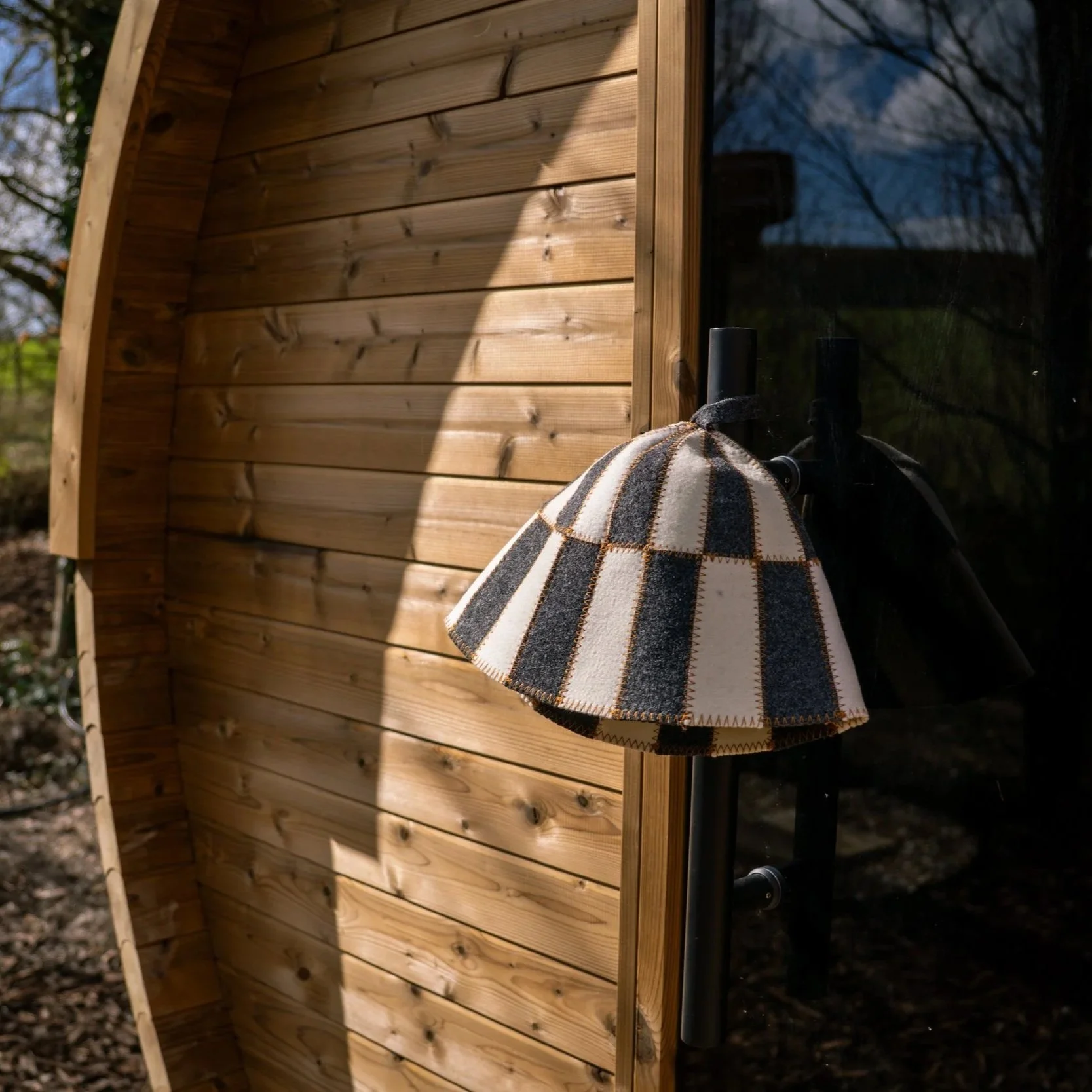 Close-up of a wall-mounted outdoor lamp with a striped fabric shade in front of a wooden wall, casting a shadow.