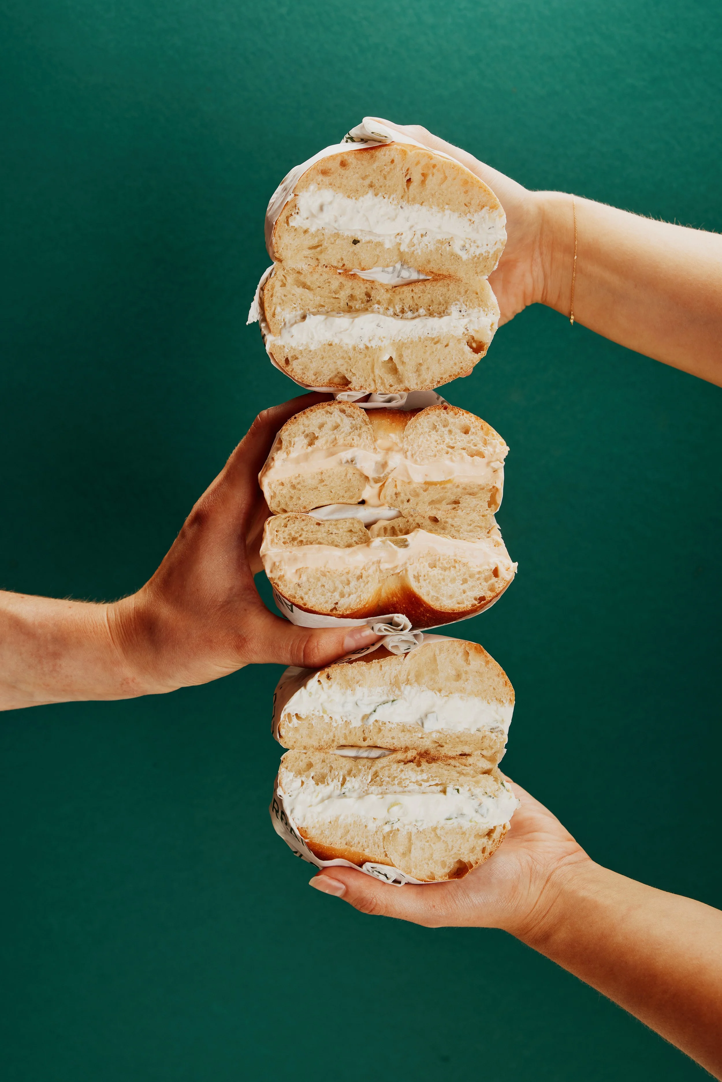 Multiple hands holding halved sponge cakes with cream filling against a green background.