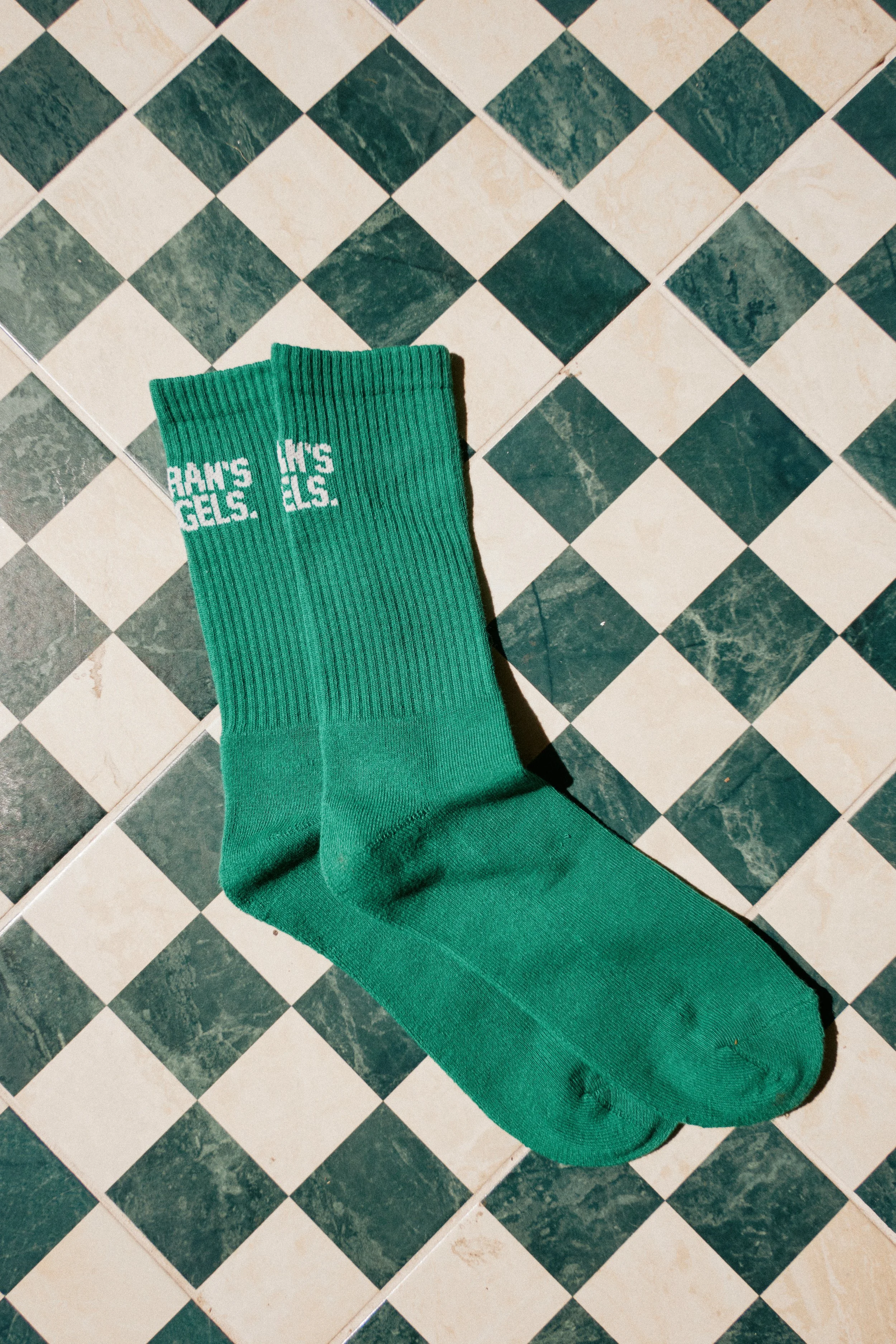 A green sock with white text on it is on a black and white checkered floor. The sock has the words "RAMS GELS" printed on it.