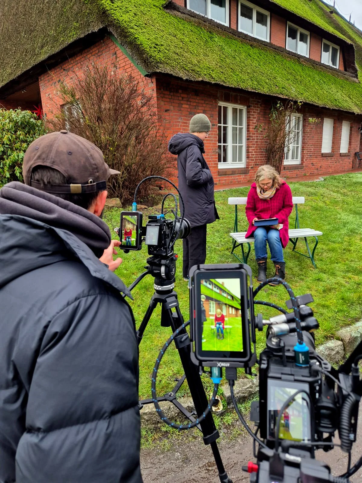 Das Team auf einem Video Dreh. Im Mittelpunkt steht die Kamera, die auf eine sitzende Frau mit Rotem Mantel gerichtet ist.
