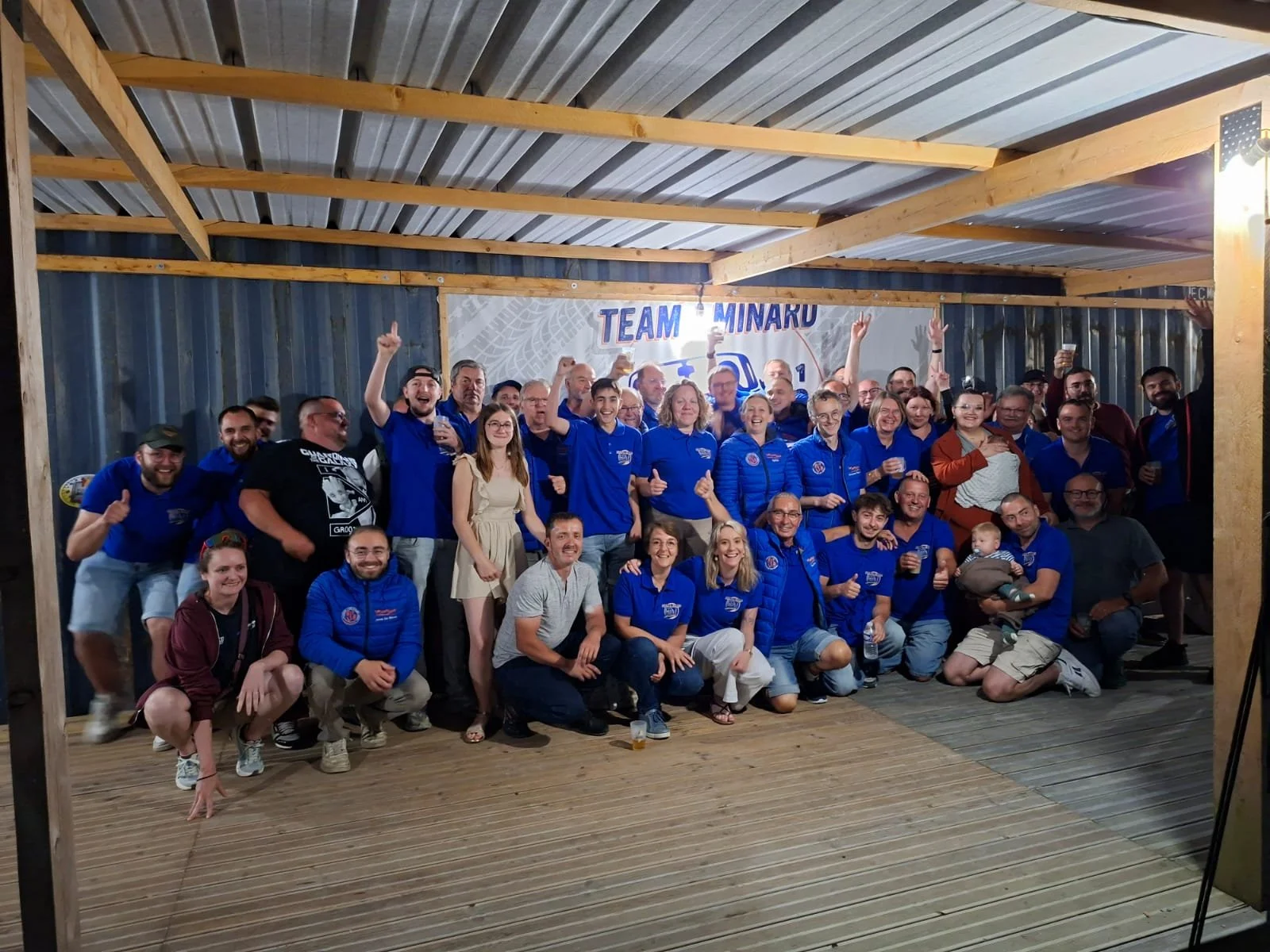 Groupe de personnes souriantes posant pour une photo lors d'un événement, avec panneau en arrière-plan indiquant 'TEAM MINARD'.