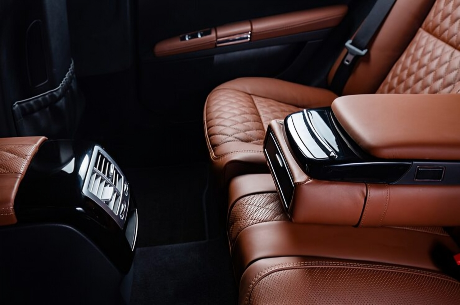 Interior of a luxury car showing brown leather seats with quilted stitching, a center console, and rear air vents.