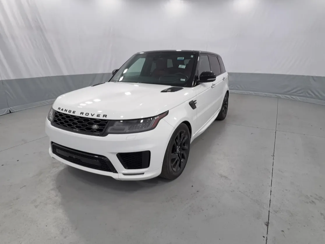 White Range Rover SUV with black accents parked in an indoor space with a gray concrete floor and a light gray curtain background.
