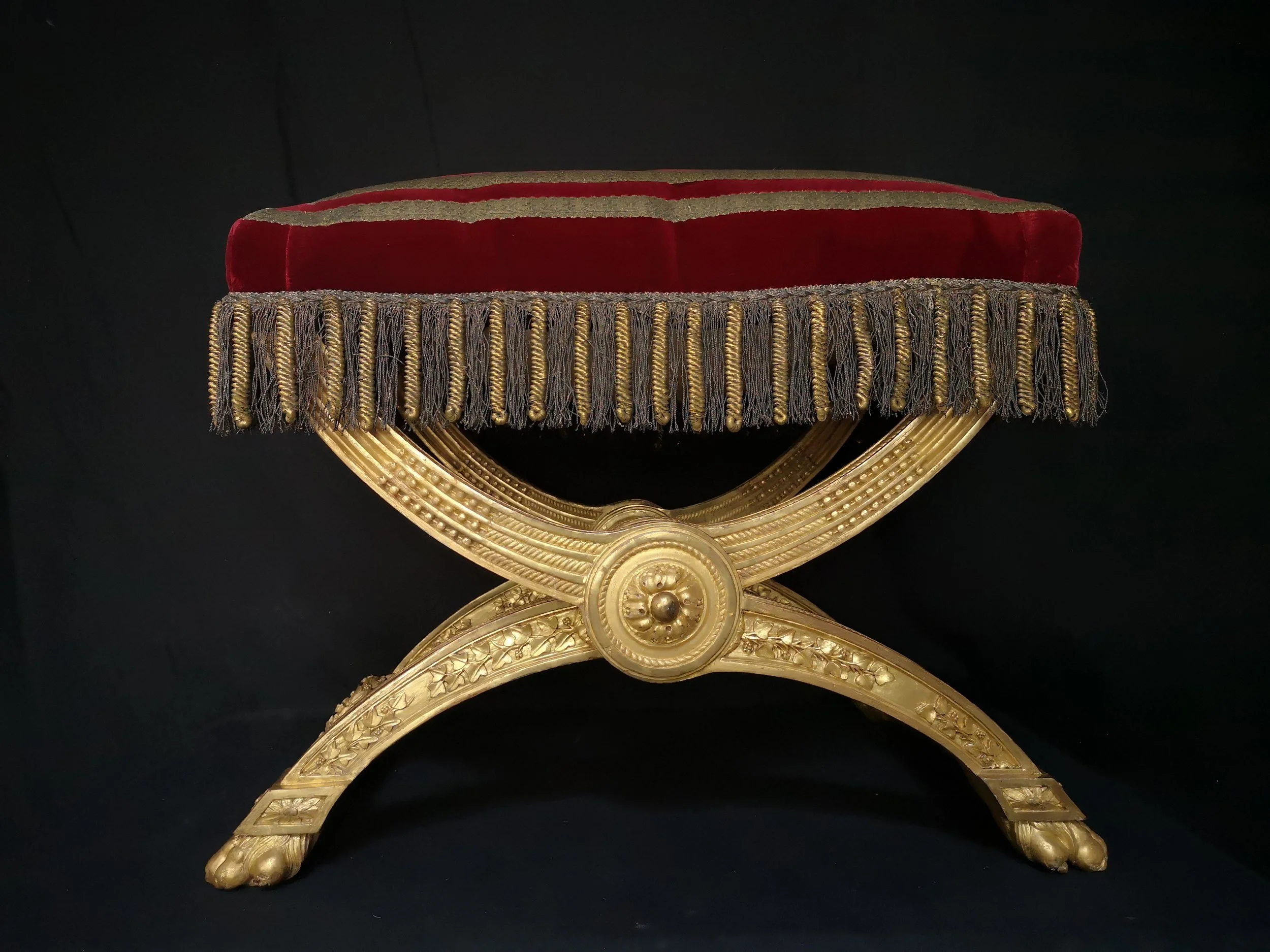 Un trône en or avec un coussin en velours rouge et des pampilles, orné de motifs détaillés et reposant sur une base en forme de patte.