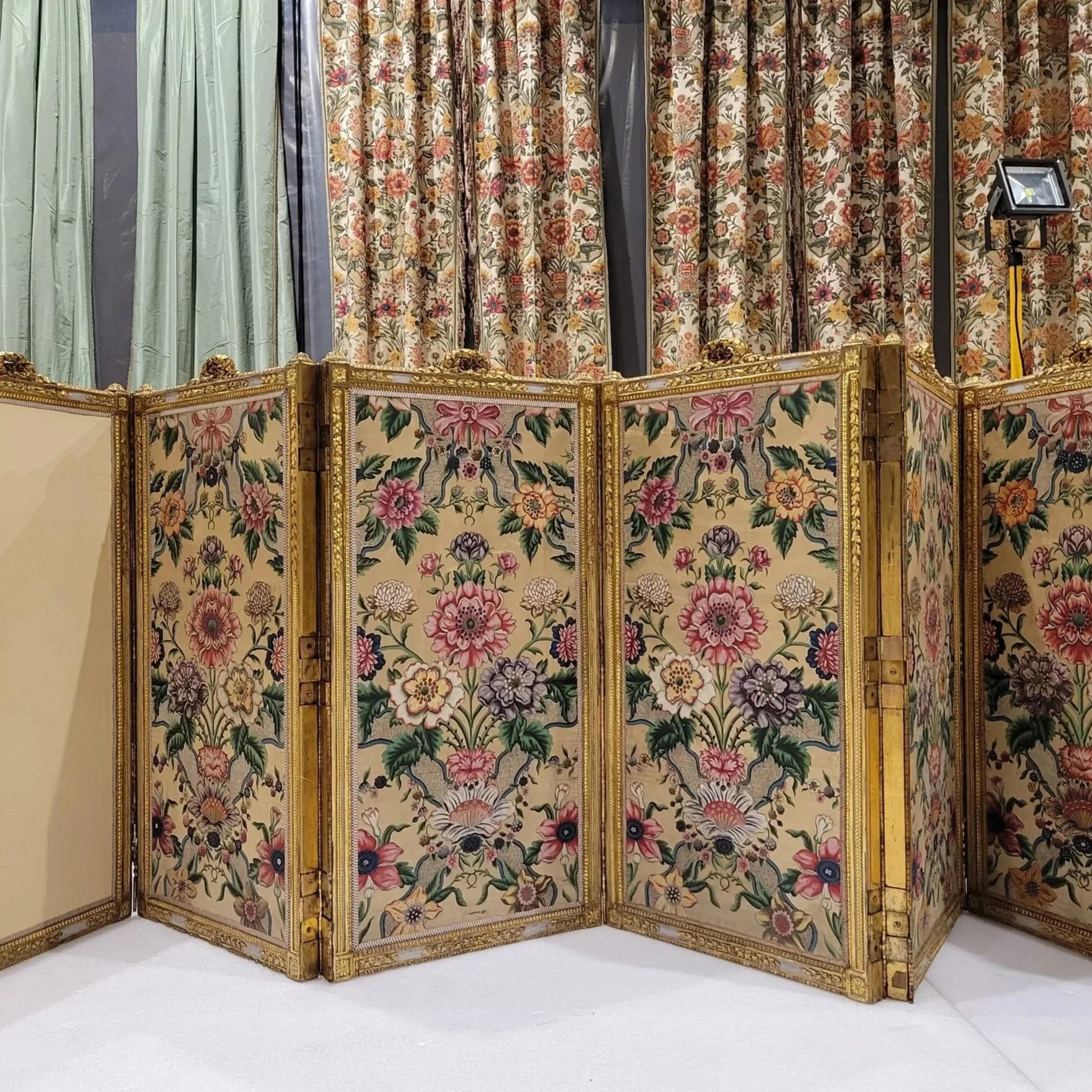 Partition décorée avec des fleurs colorées et un cadre doré, utilisée comme paravent dans une salle d'exposition ou musée.