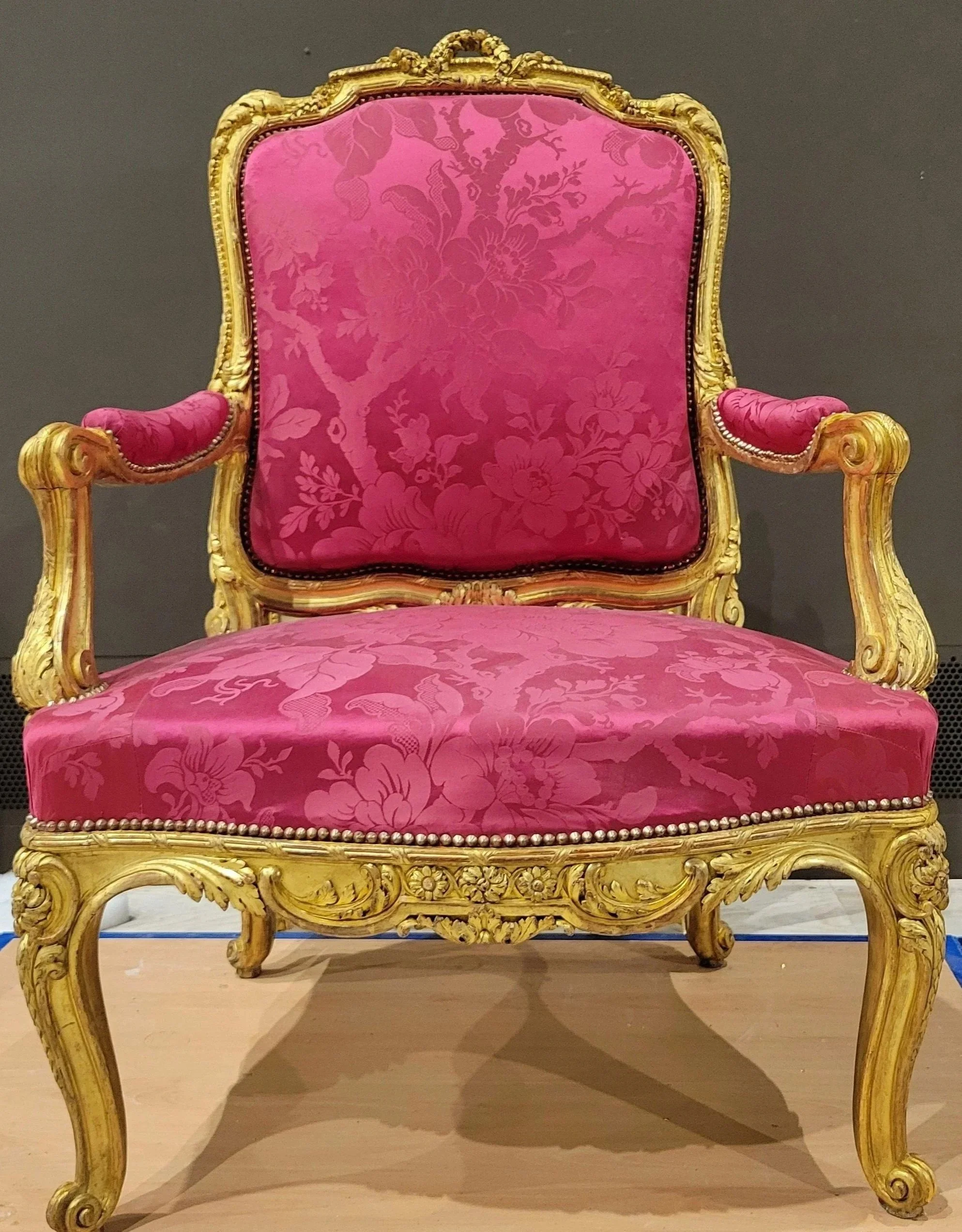 Fauteuil de style louis XV orné de bois doré et tapisserie rose avec motif floral.