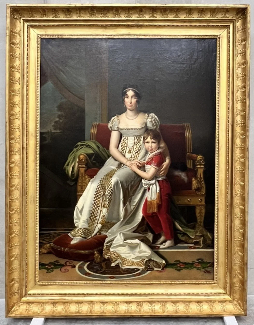 Peinture représentant deux femmes, l'une assise et l'autre adulte, dans un cadre doré ornée. L'une porte une robe élégante et l'autre une robe rouge, dans un style classique.
