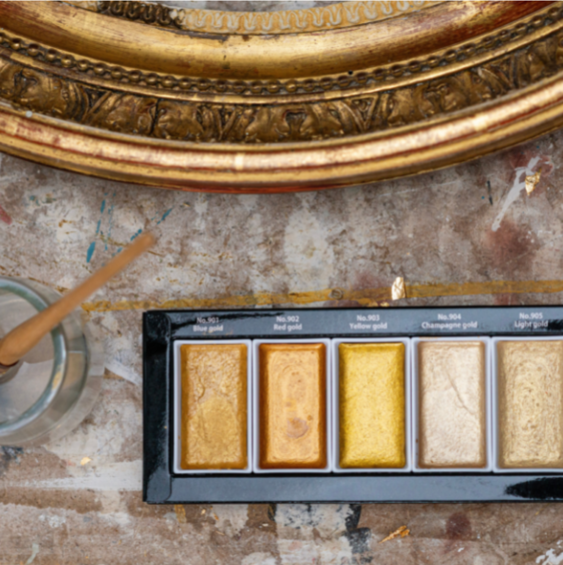 Palette de pastels colorés pour peinture, avec des teintes dorées et jaunes, posée sur une surface de travail usée.