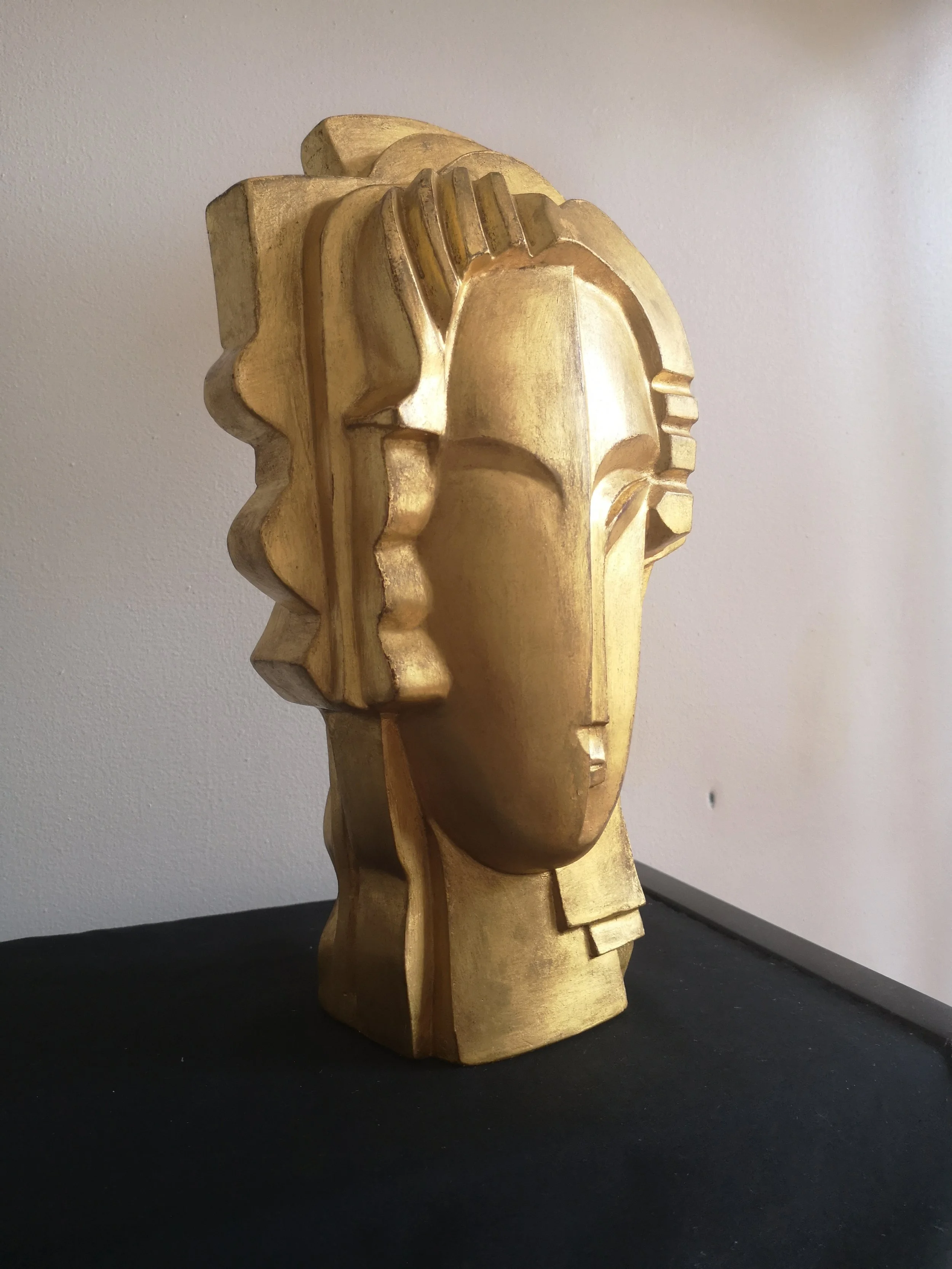 Sculpture en bois représentant une tête stylisée aux caractéristiques géométriques et abstraites posée sur une surface noire.