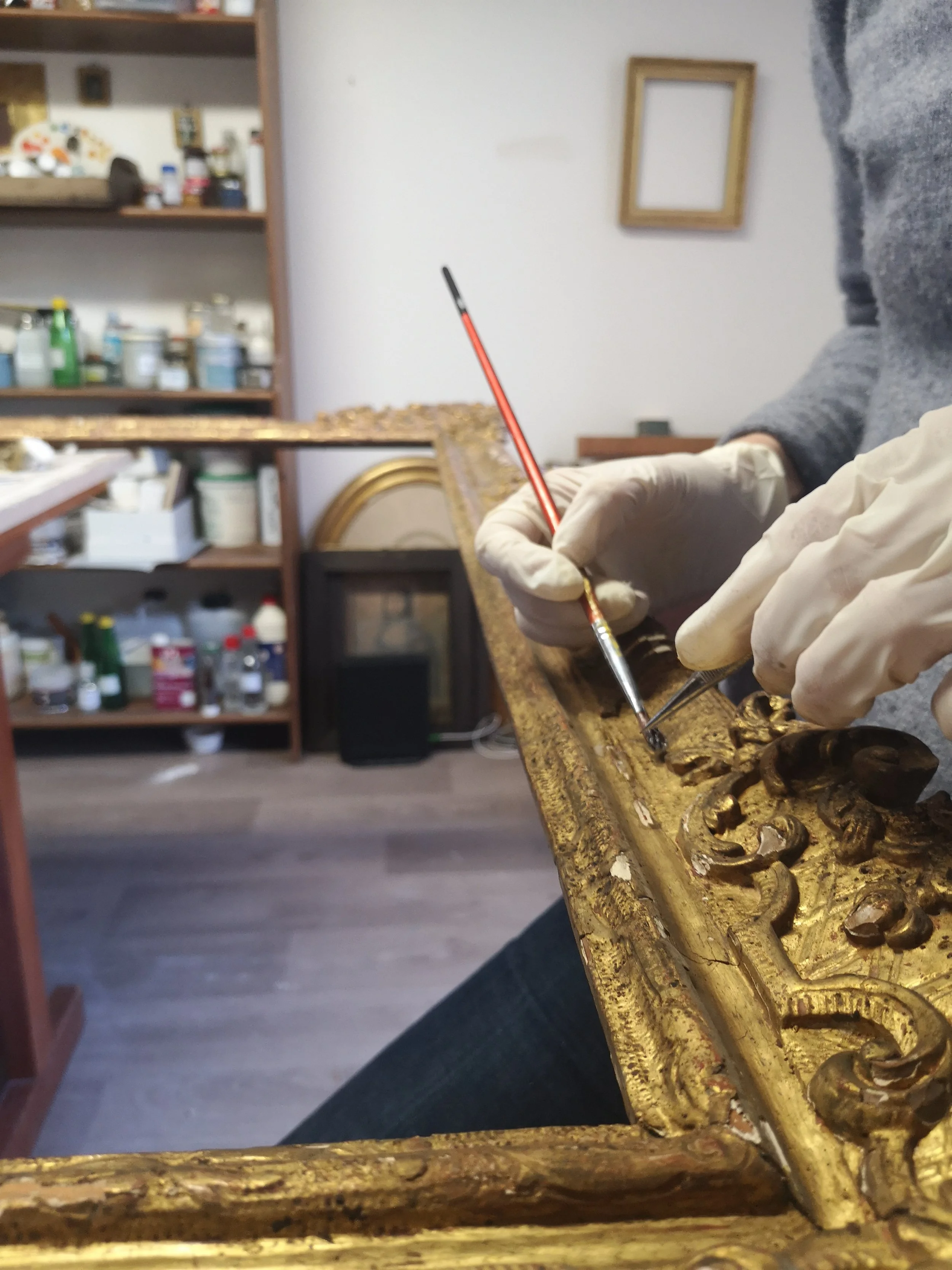 Une personne en train de restaurer ou de toucher une pièce d'art ancien en bois doré avec des outils, dans un atelier.