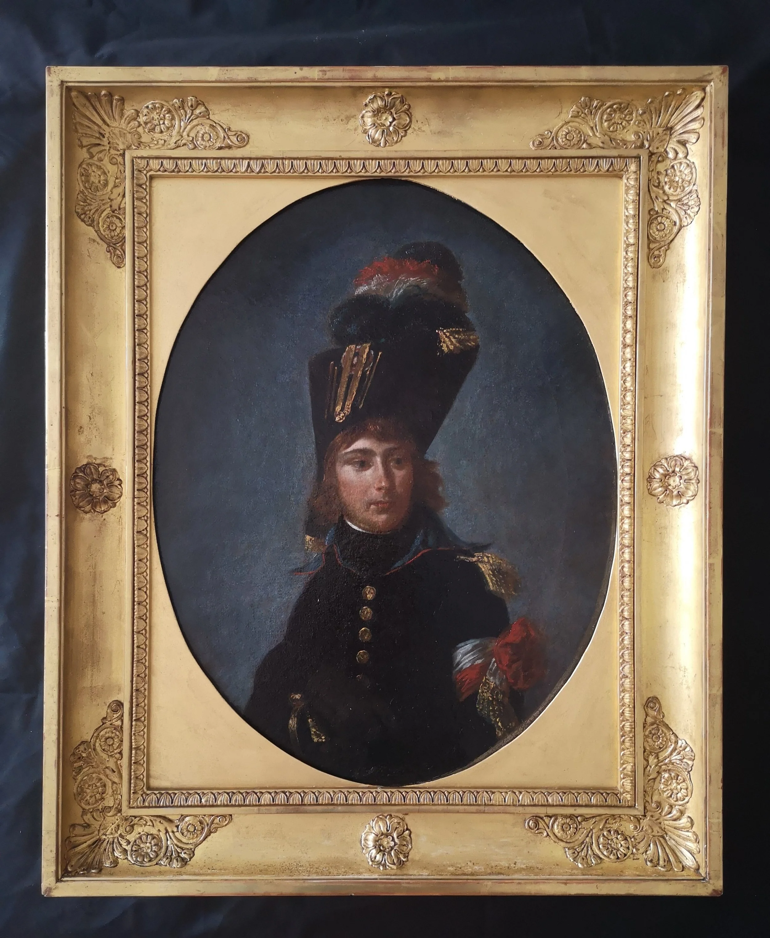 Peinture d'un personnage en uniforme militaire dans un cadre orné avec des motifs floraux.