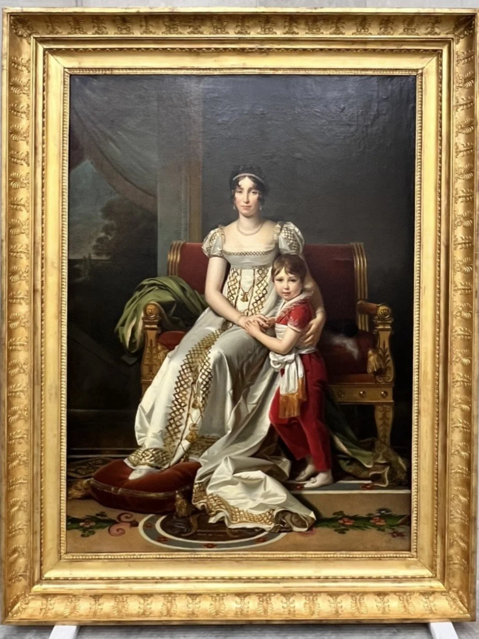 Peinture représentant une femme assise sur un fauteuil avec un jeune garçon à ses côtés, avec un cadre doré orné.
