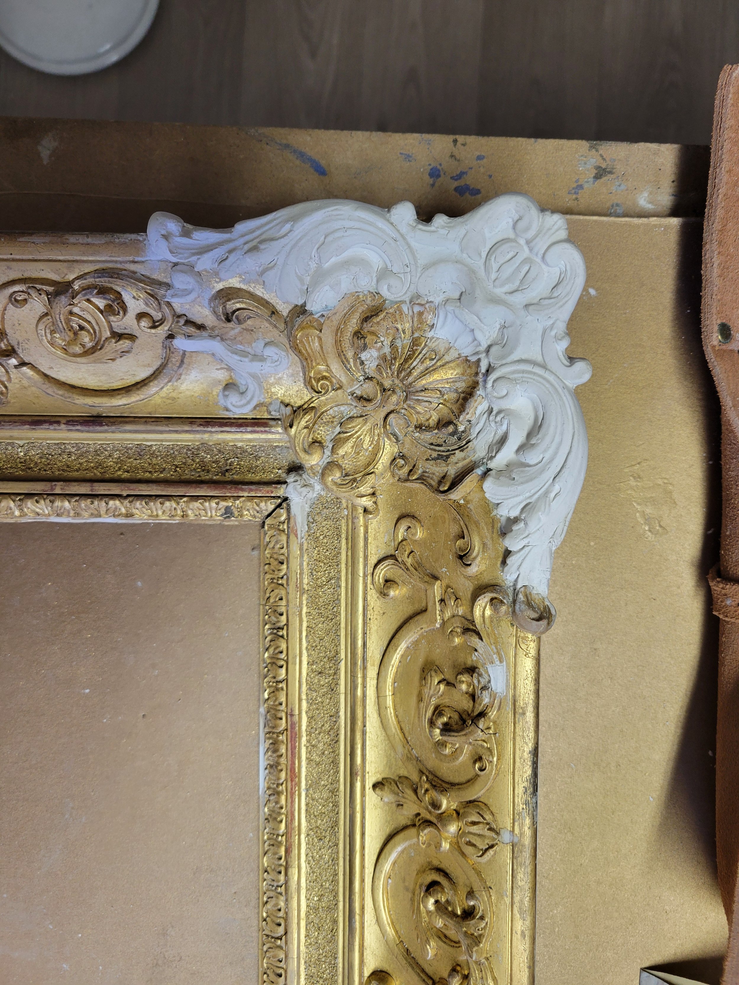 Décoration murale ornée de sculptures en bois ou en plâtre avec des motifs baroques en blanc et doré, partie d'un cadre ou d'une moulure richement décorée.