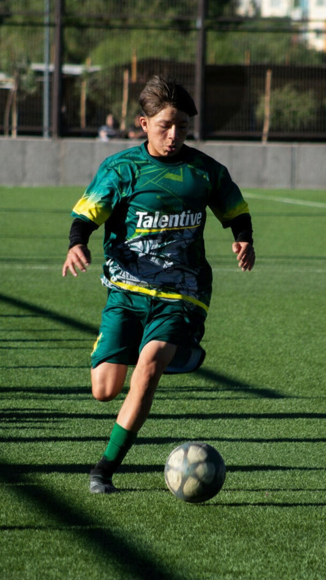 Young male soccer player in athletic uniform running on a grass field, with a soccer ball at his feet.
