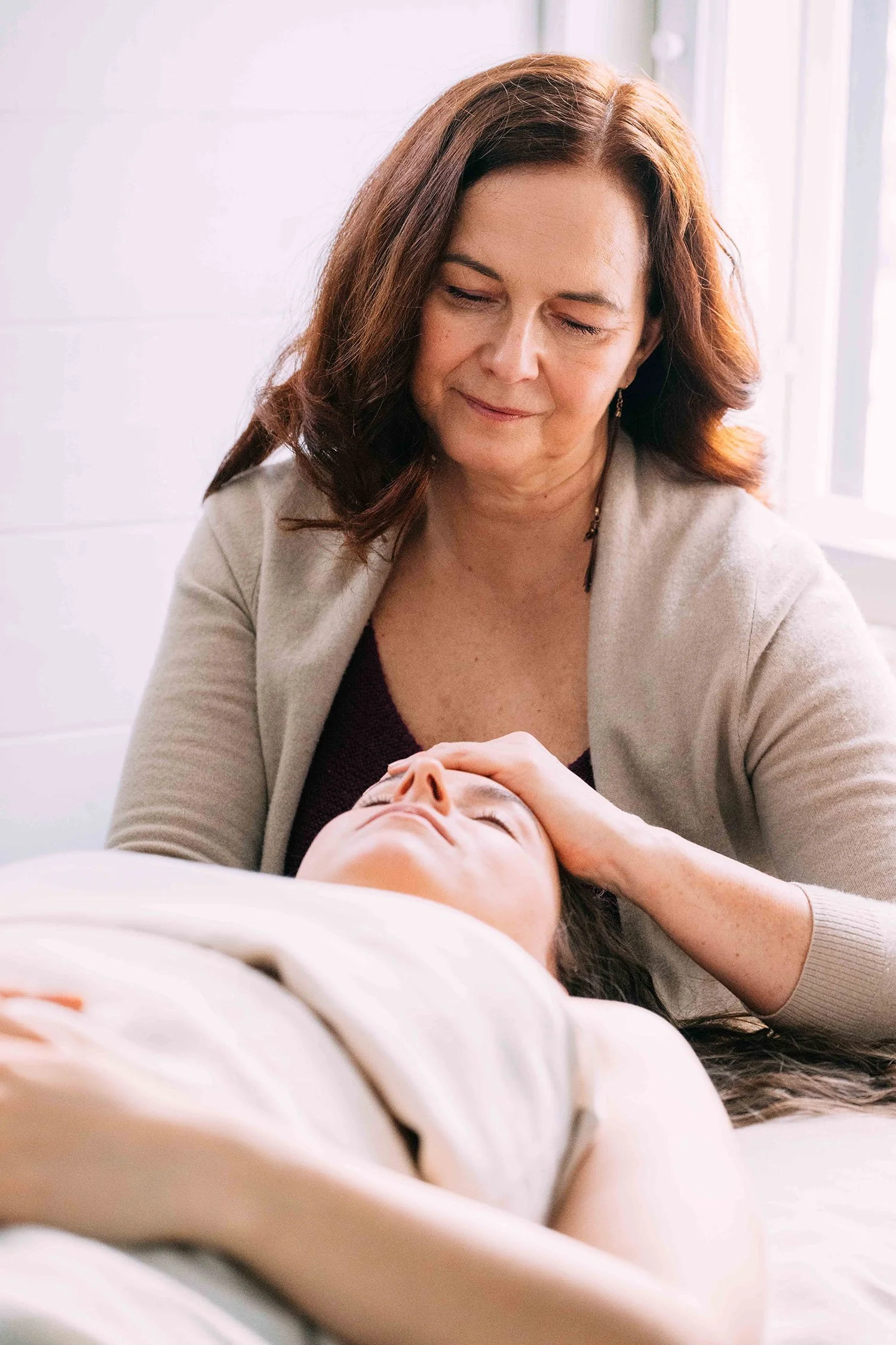 Kehon aalloilla Rosen-terapeutti koskettaa selinmakuulla olevan asiakkaan otsaa.