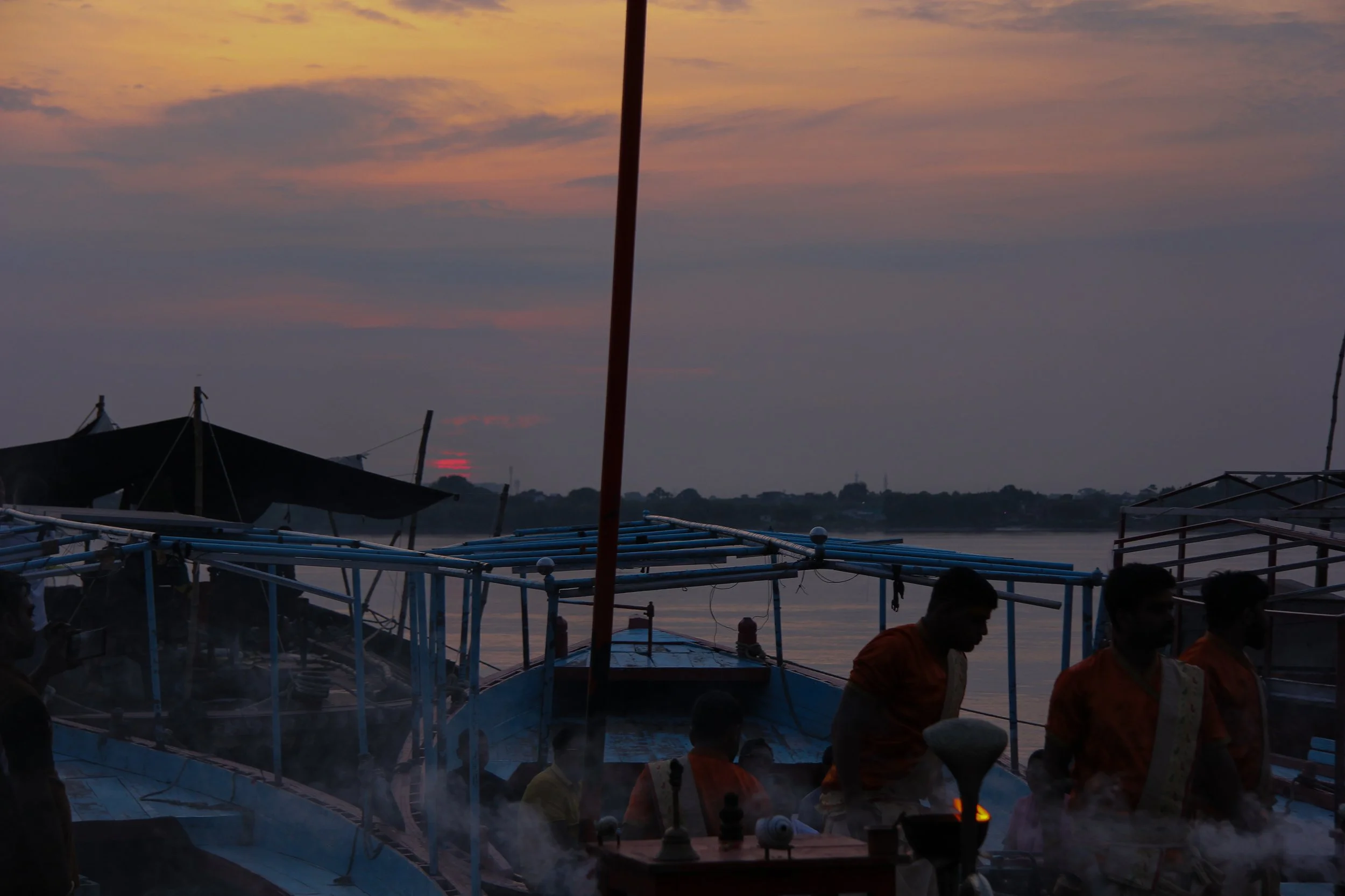 Silhouettes of people on boats during sunset with a sky filled with orange and purple hues.