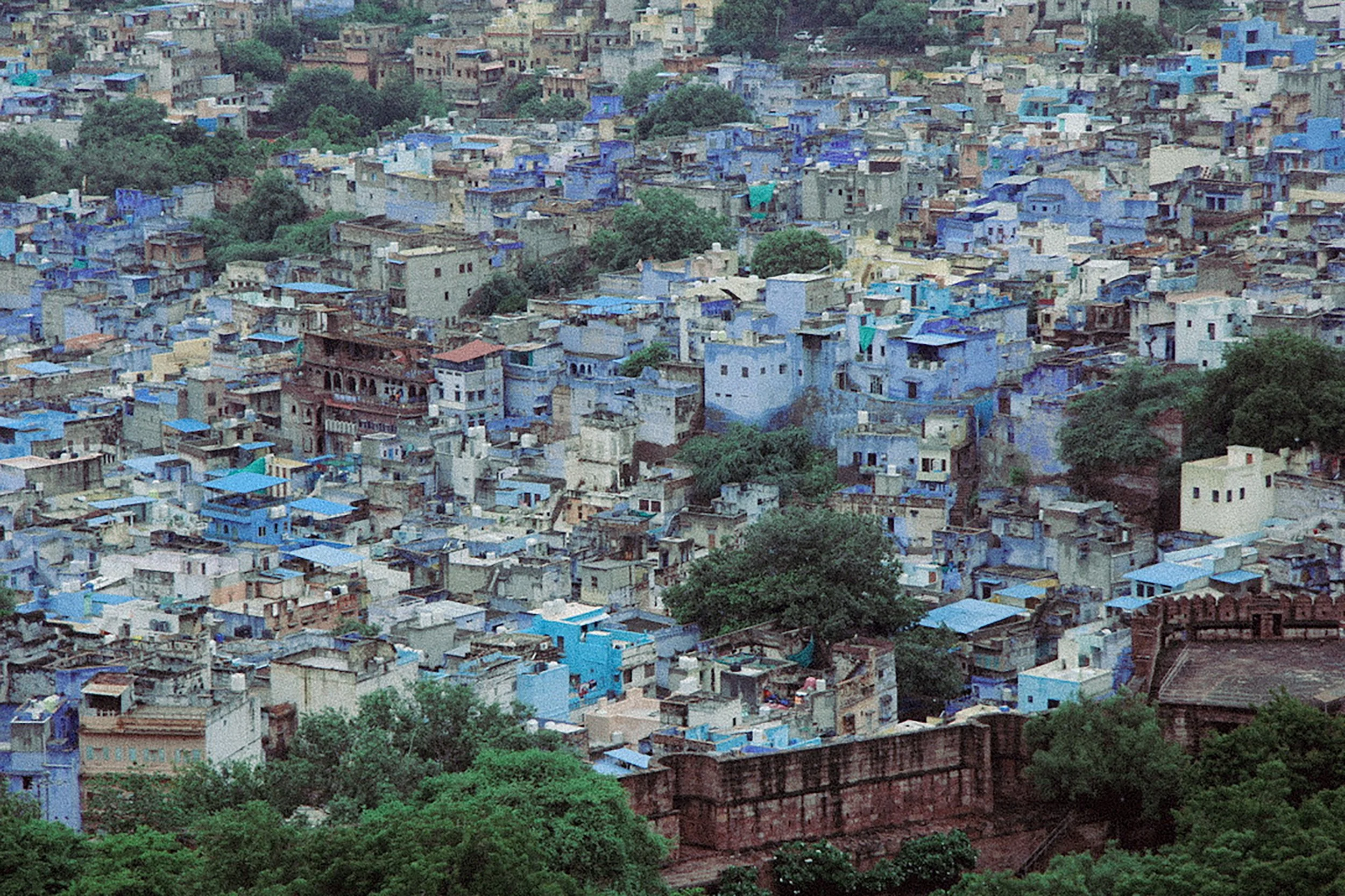 A densely packed hillside of colored buildings, predominantly in shades of blue, with some greenery and trees interspersed among the structures.
