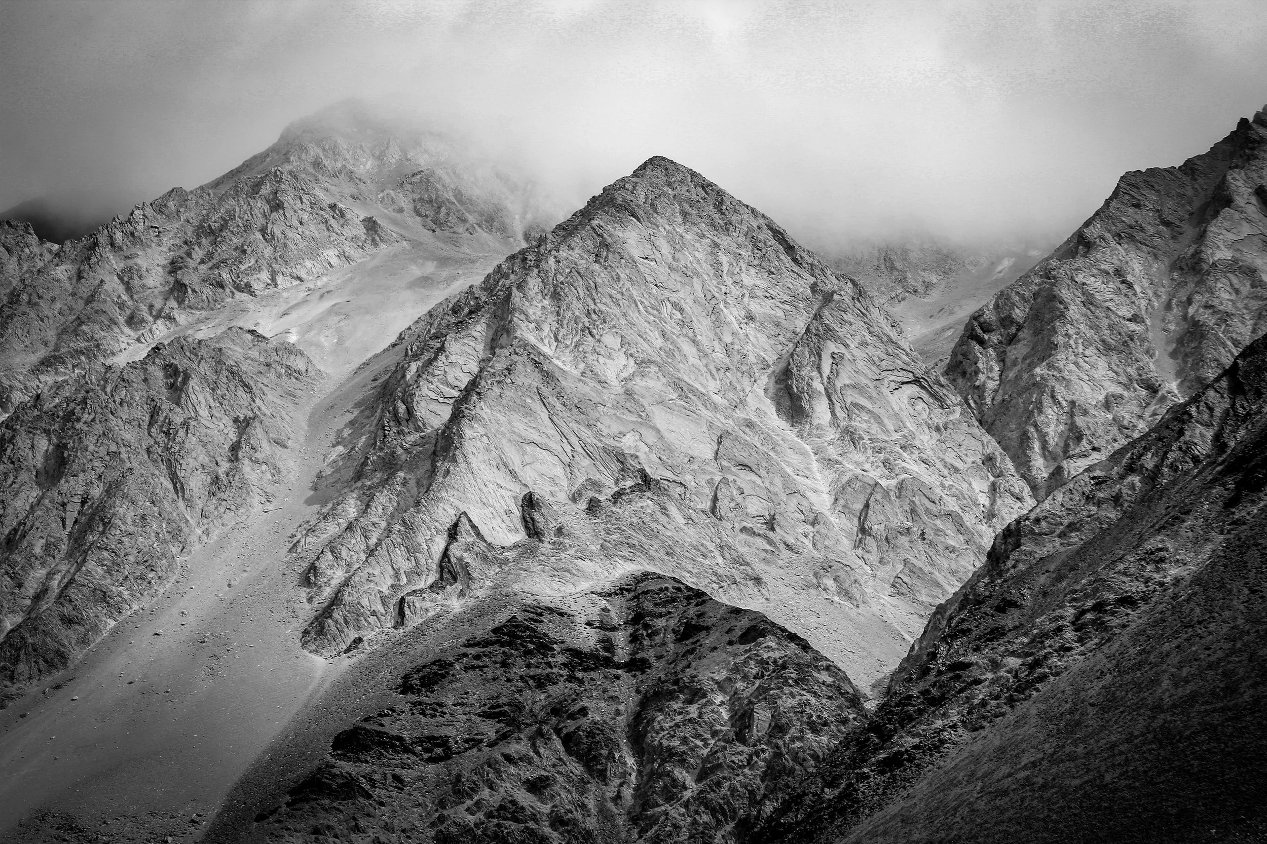 Black and white photograph of rugged mountain peaks with clouds surrounding the summits.