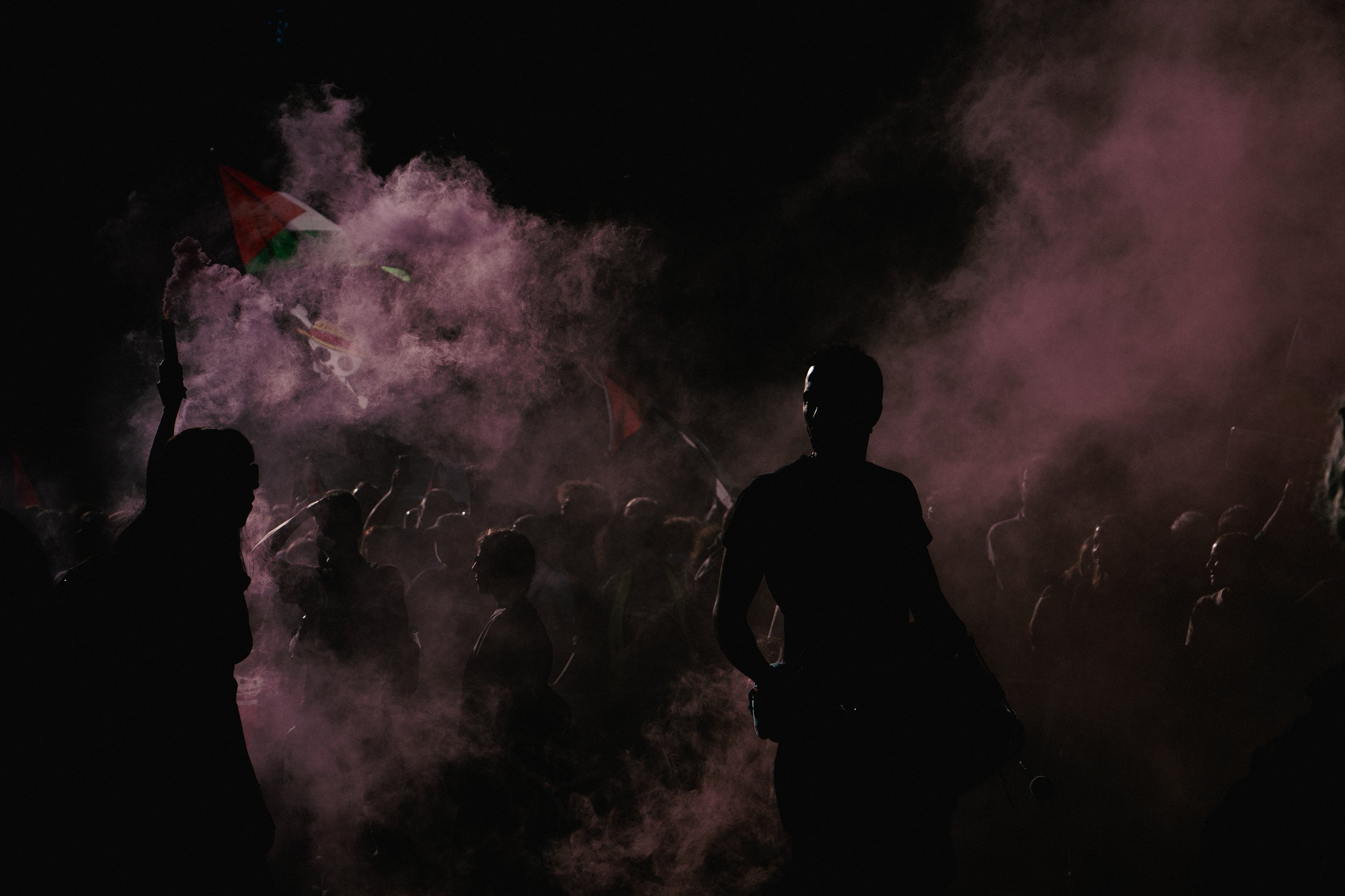 Silhouettes of people at night with pink smoke and flags.