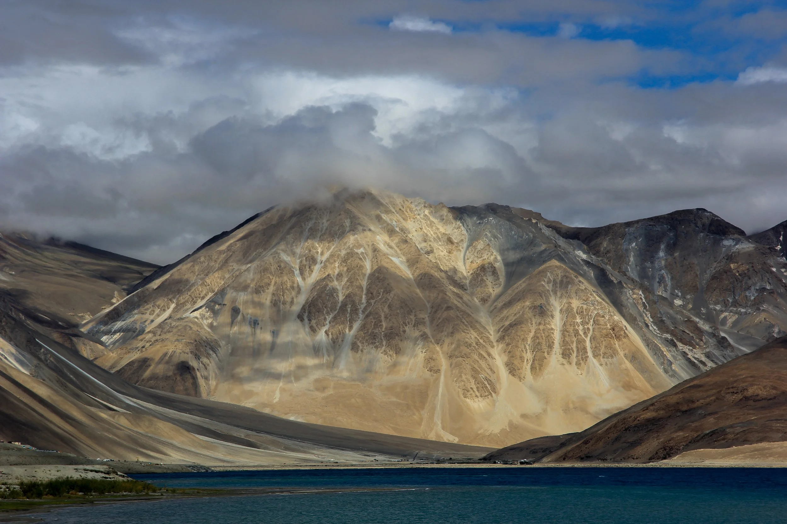 Scenic view of a large mountainous landscape with a lake in the foreground, partly cloudy sky overhead.
