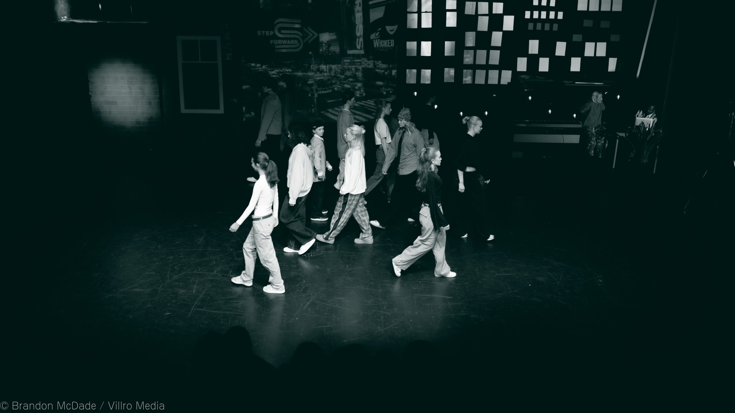 Group of young dancers practicing on a stage with a cityscape backdrop.