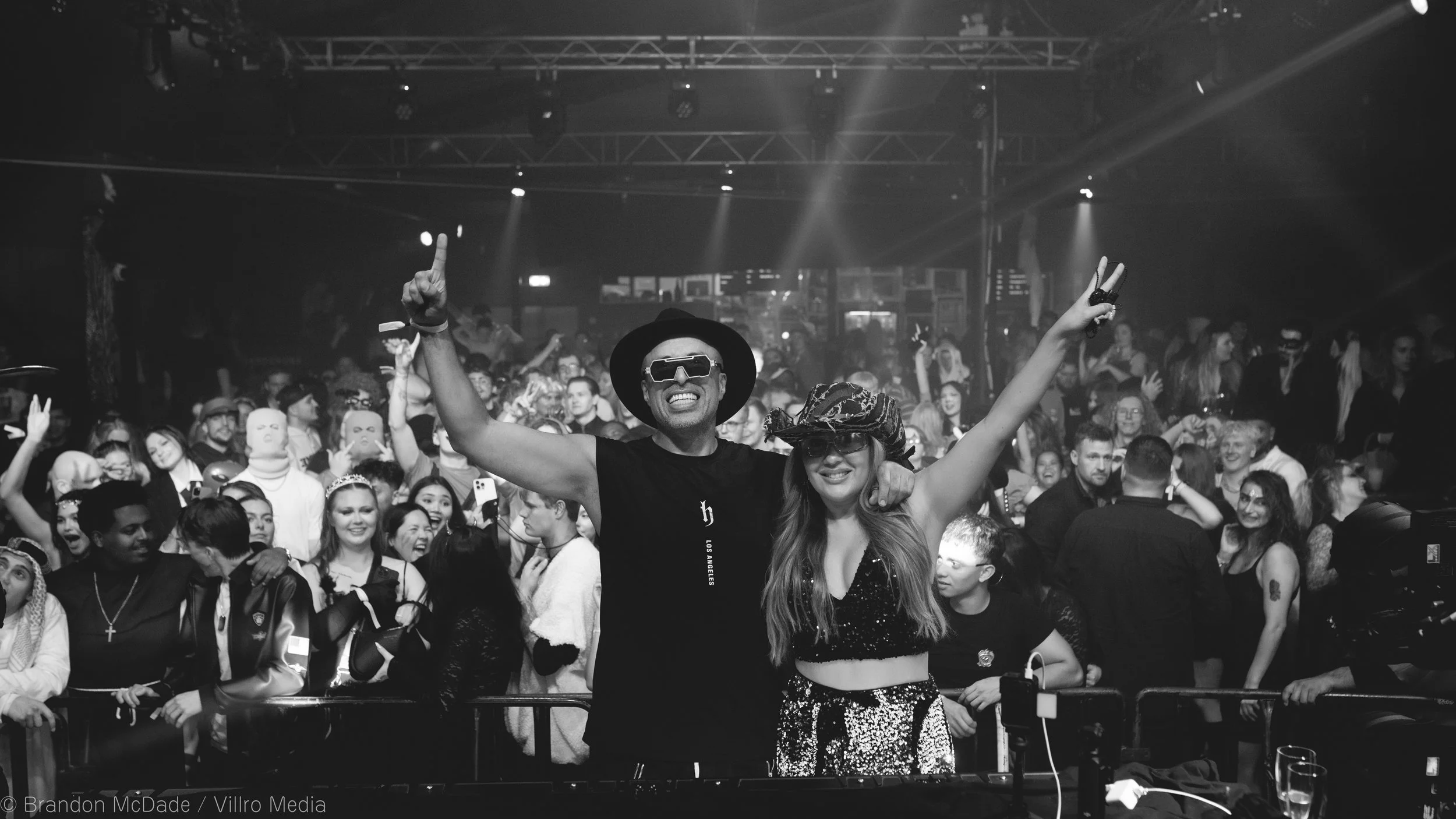 People dancing and celebrating at a concert or club, with some individuals wearing masks and costumes, capturing a lively, energetic atmosphere.