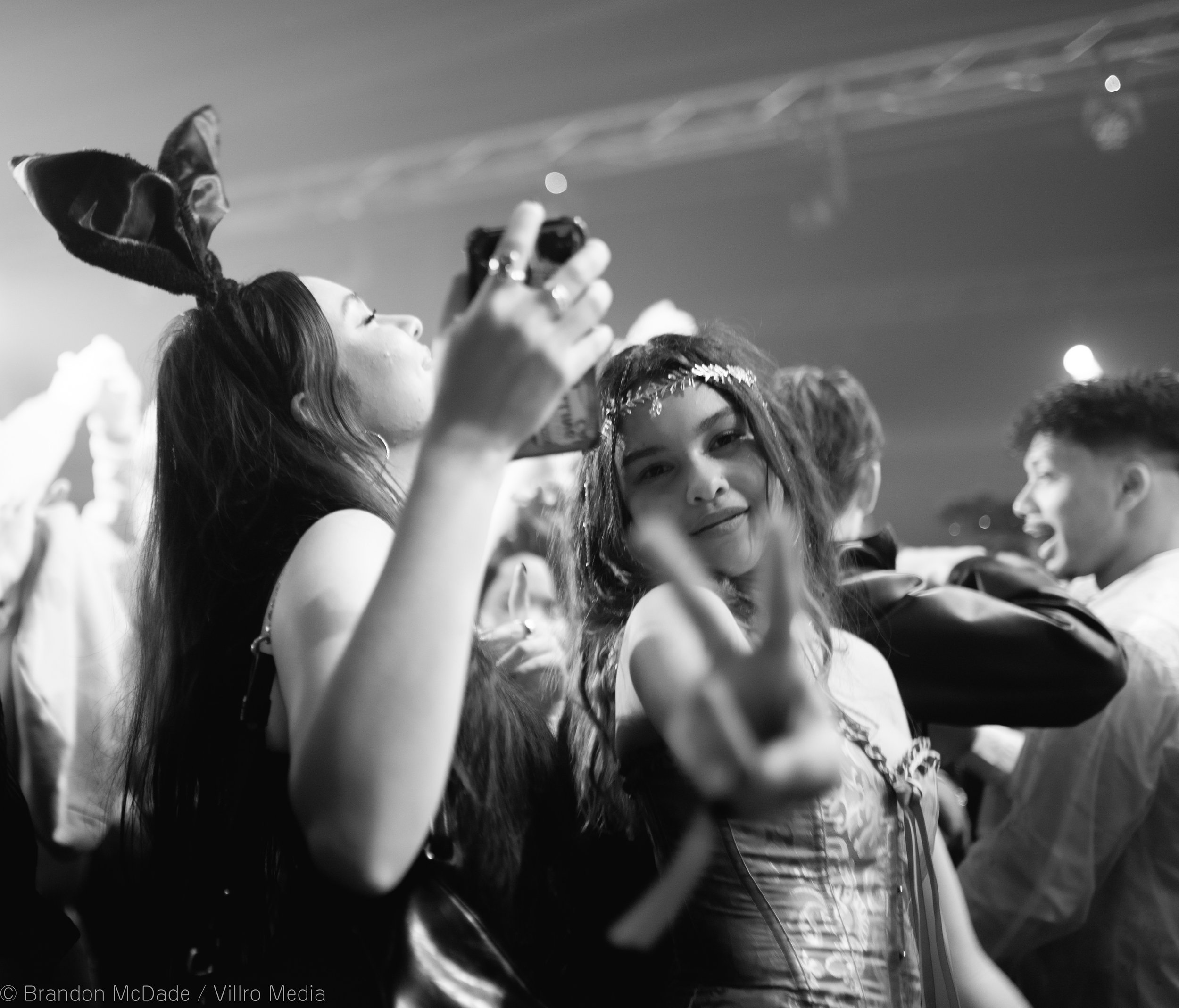 People at a party, some dressed in costumes, with one woman in the foreground making a peace sign and smiling.
