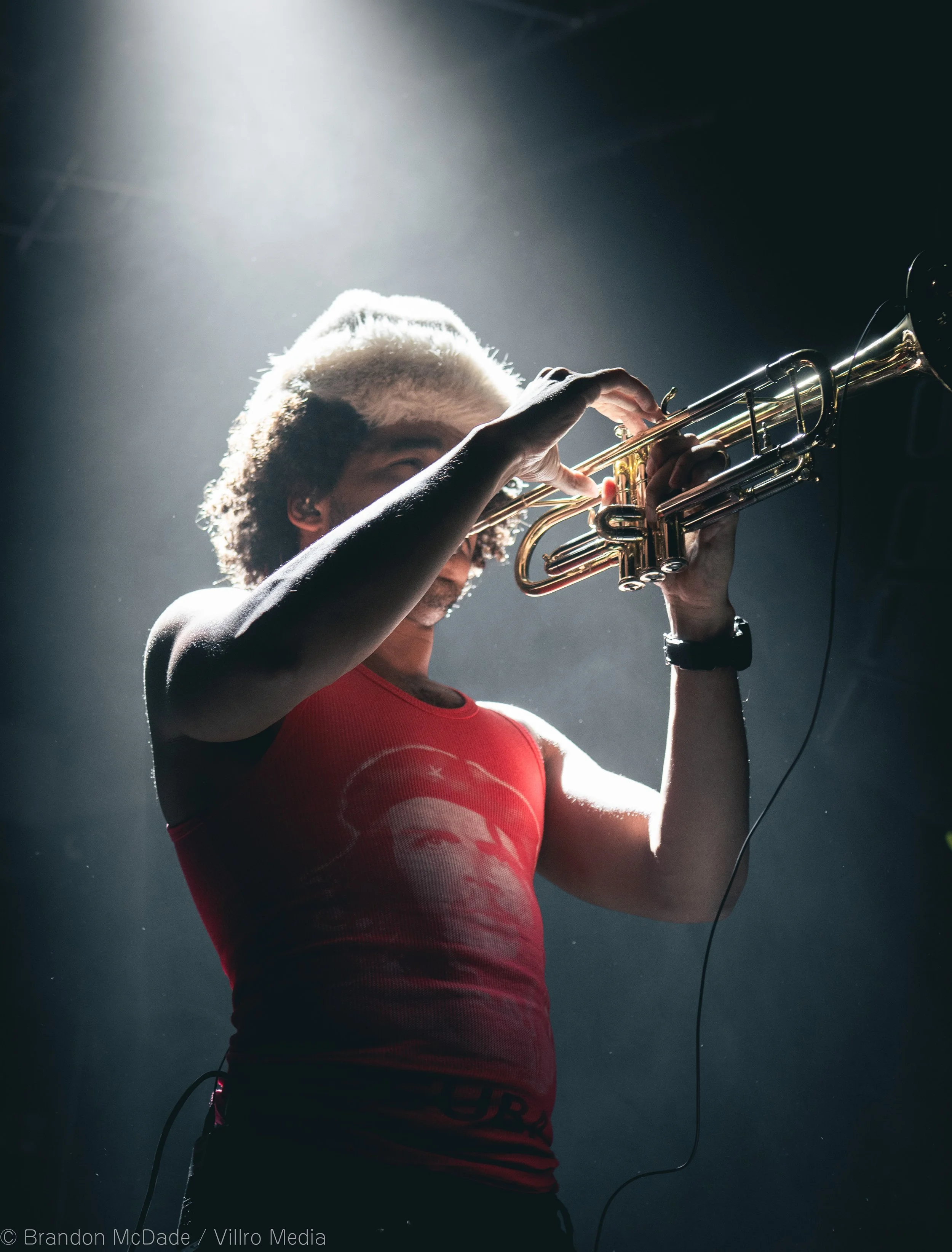 Person playing a trumpet on stage, with dramatic lighting highlighting their hair and upper body.