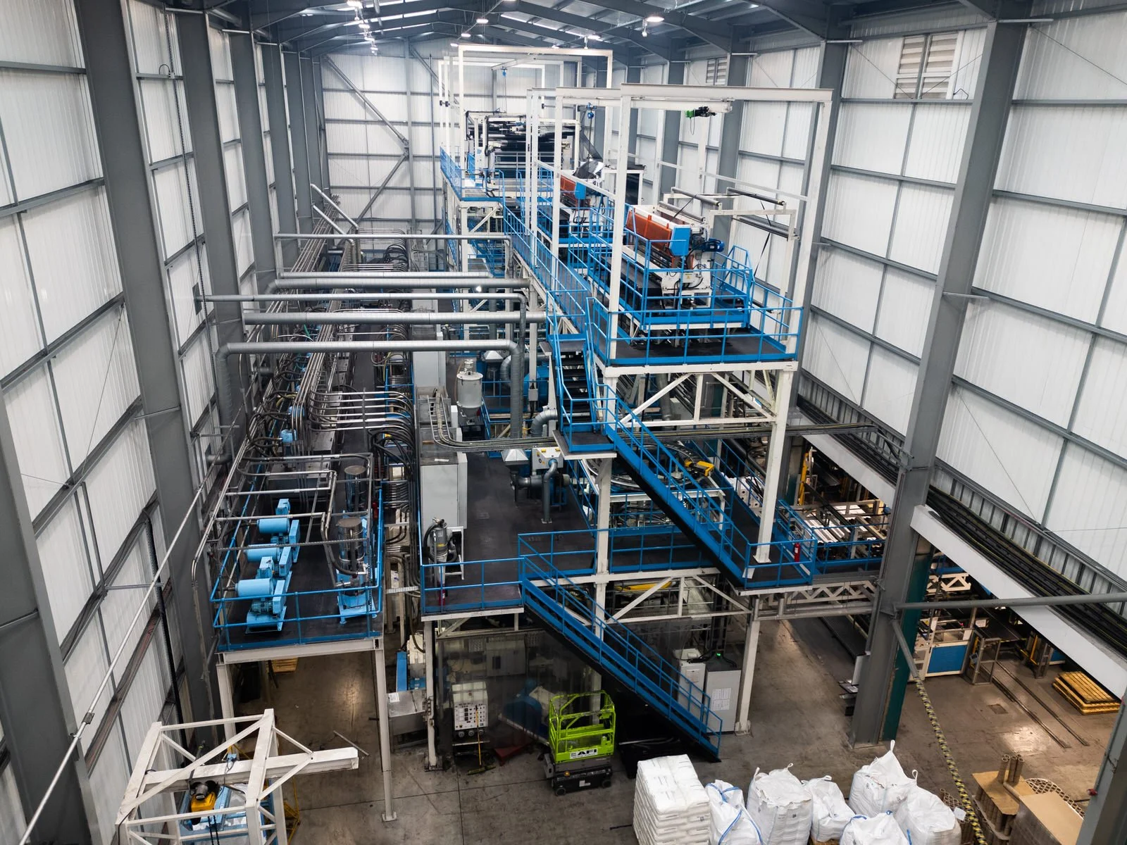 Interior view of an industrial facility with metal pipes, ladders, and machinery inside a large warehouse.