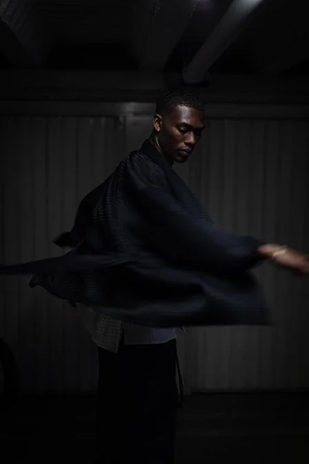A person wearing a black kimoni is spinning in a dimly lit room, with motion blur visible on their arms.