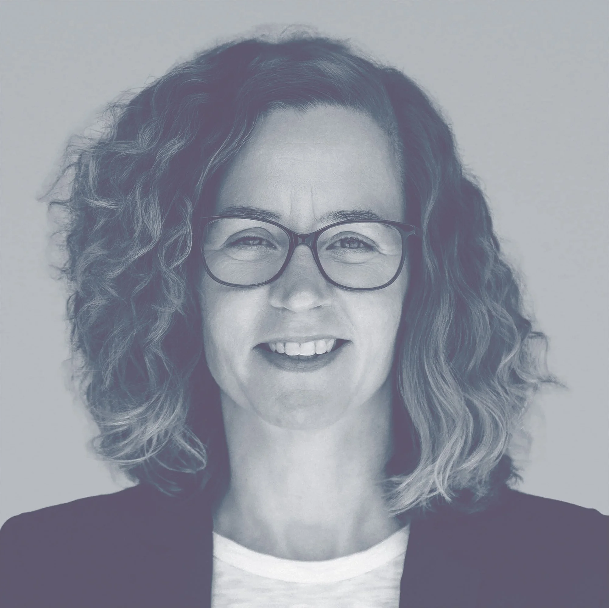 Porträt einer lächelnden Frau mit braunen, lockigen Haaren und Brille.