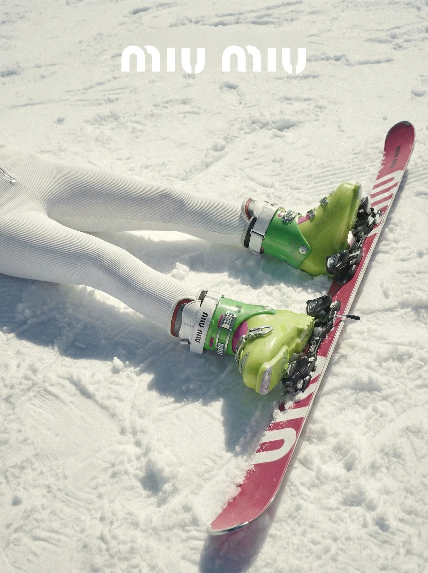 Close-up of a person's legs lying on snow with ski boots and skis, snow-covered ground, and no other objects visible.