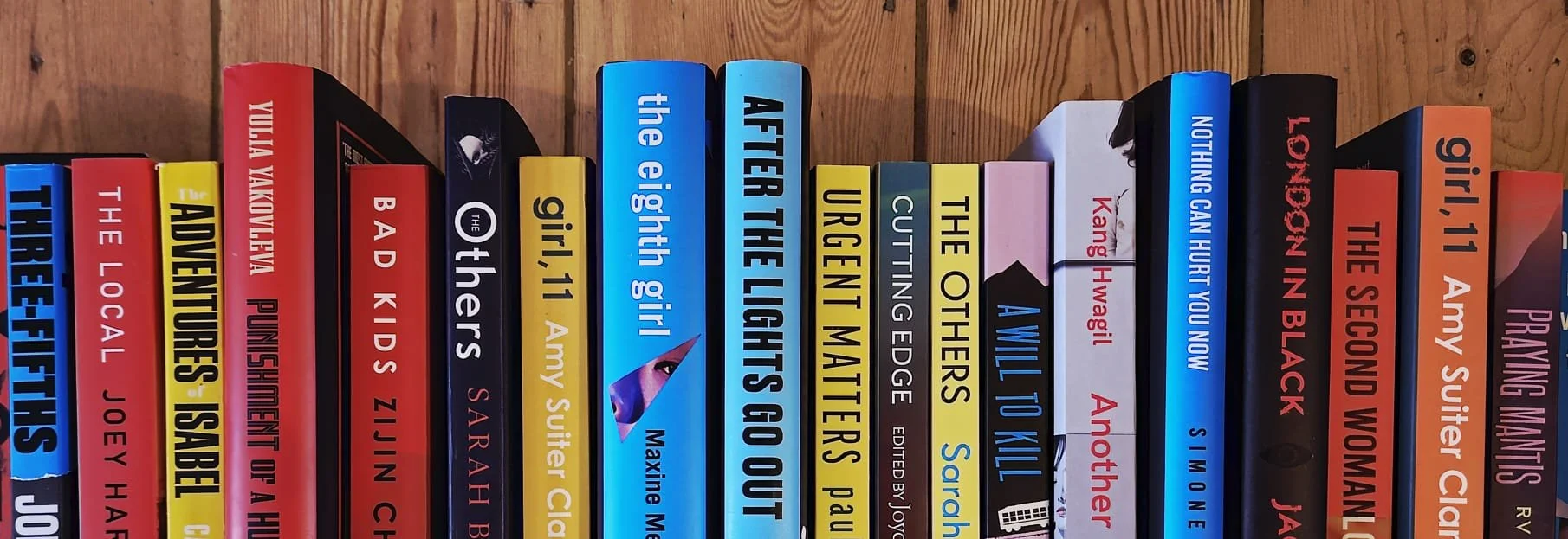 A row of books on a wooden shelf with various colored spines, titles, and authors visible.