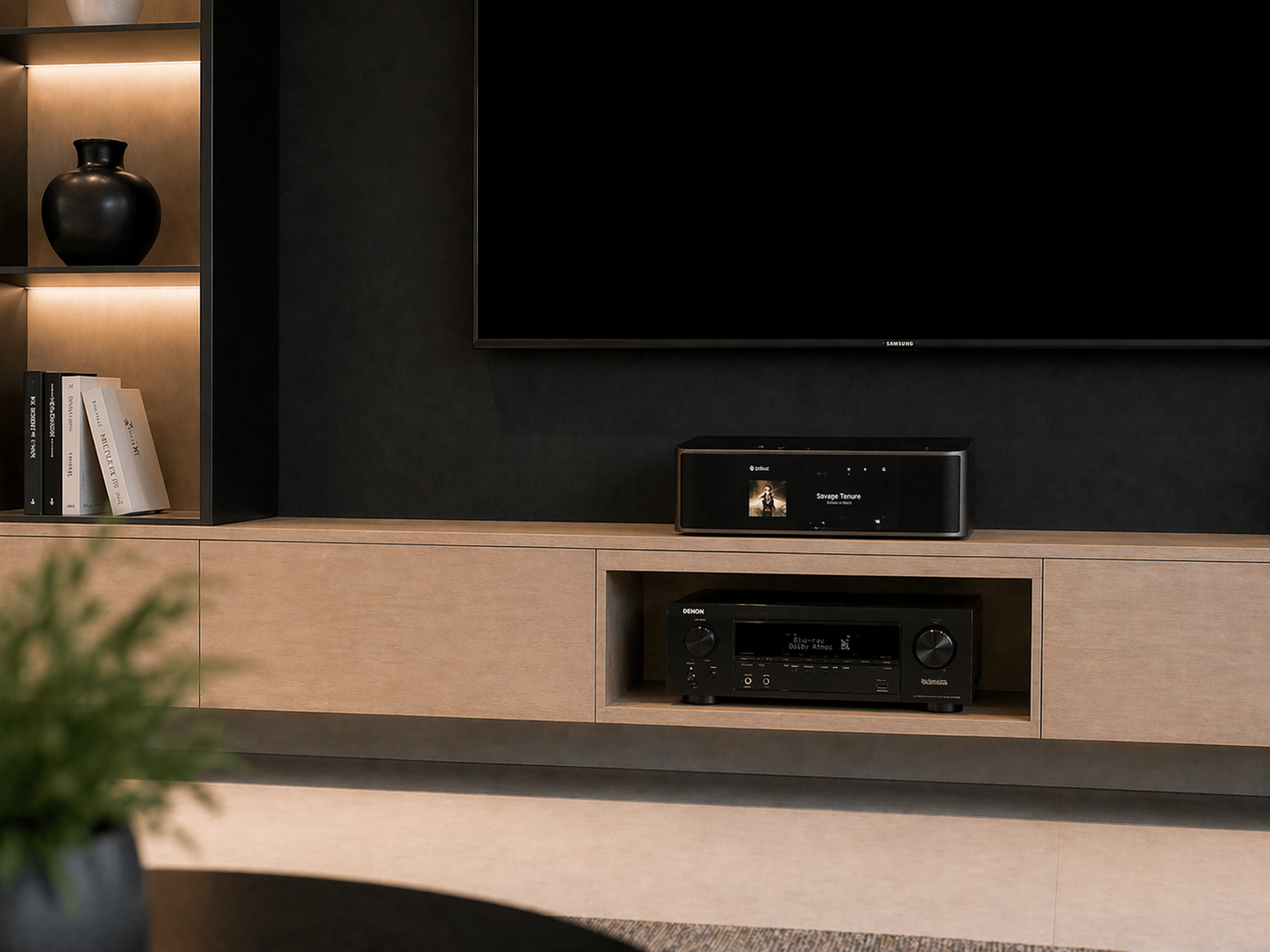 Living room entertainment center with a flat-screen TV, a speaker, a stereo receiver, a black vase, and books on a wooden shelf.