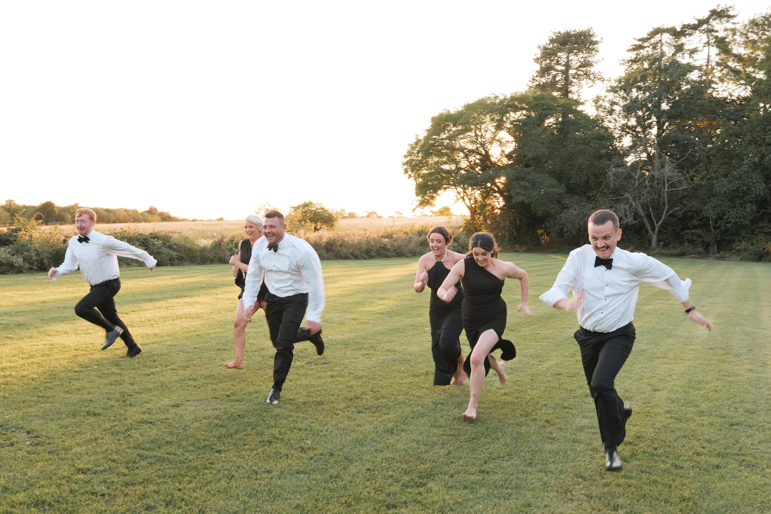 group running towards camera in black tie and gowns. golden hour