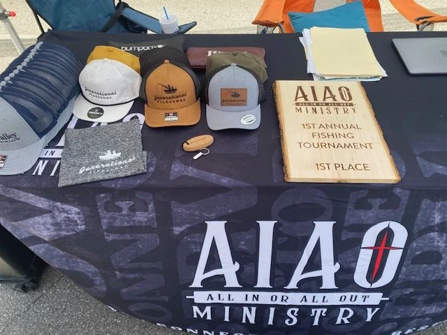 Table with hats, a plaque, and papers at a fishing tournament booth.