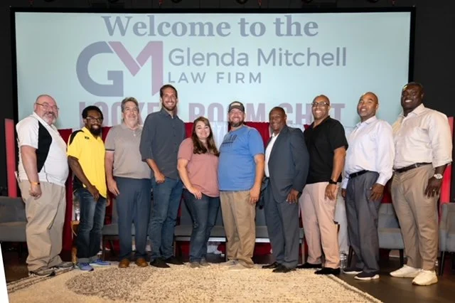 Group of ten people standing in front of a large screen displaying a welcome message for Glenda Mitchell Law Firm, with a mix of men and women dressed casually and professionally.