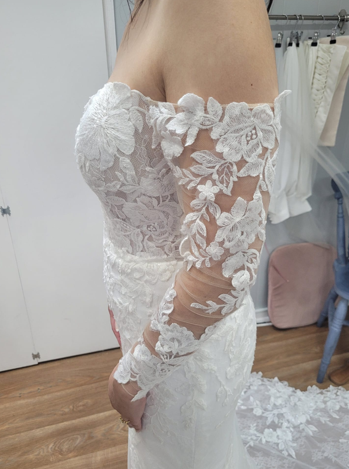 Close-up of a woman wearing an off-the-shoulder white lace wedding dress with floral embroidery.