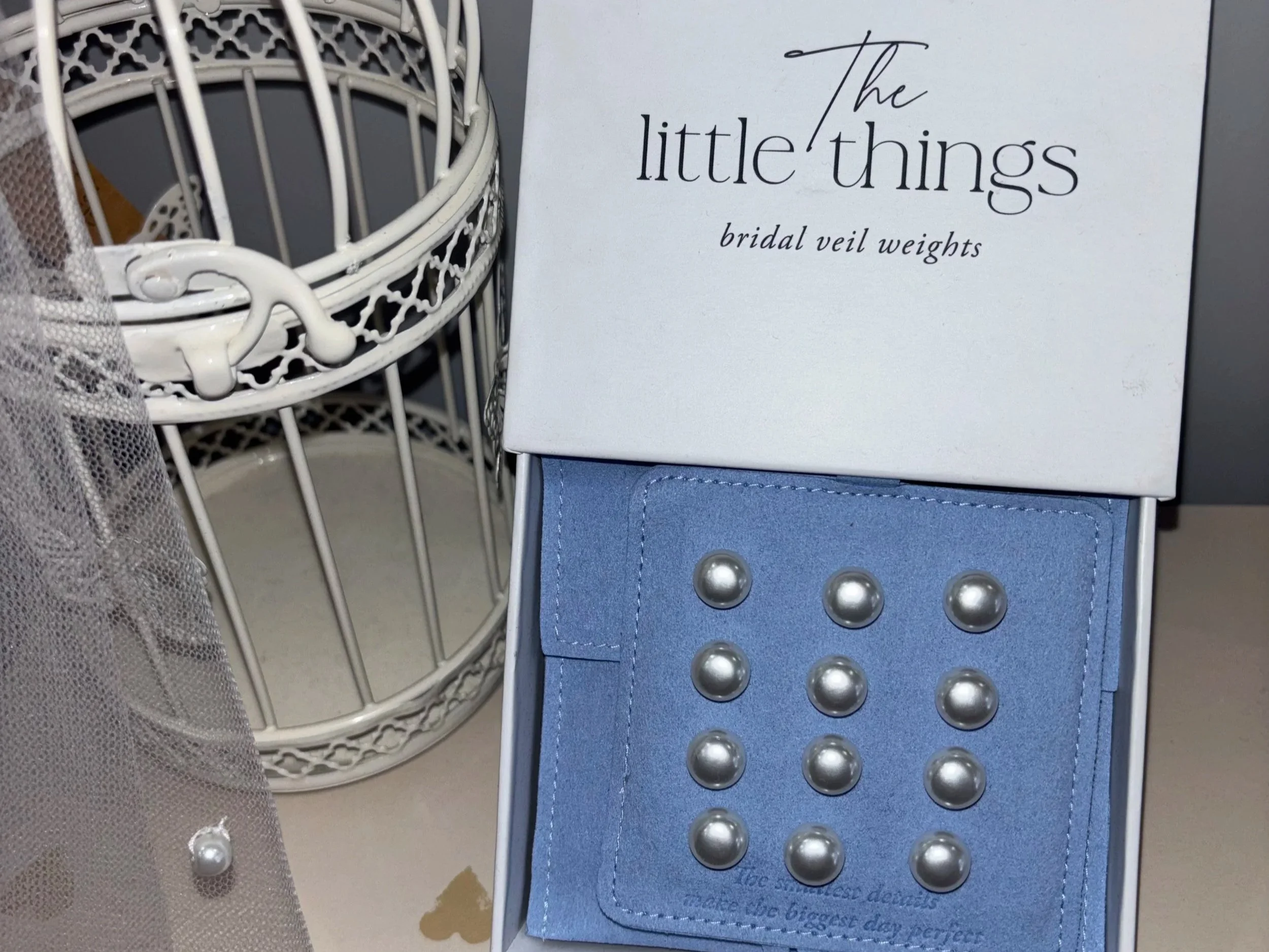 Close-up of a white decorative jewelry stand on the left and a small bridal vault weights with metallic balls on the right. Part of a blue denim fabric is visible at the bottom.