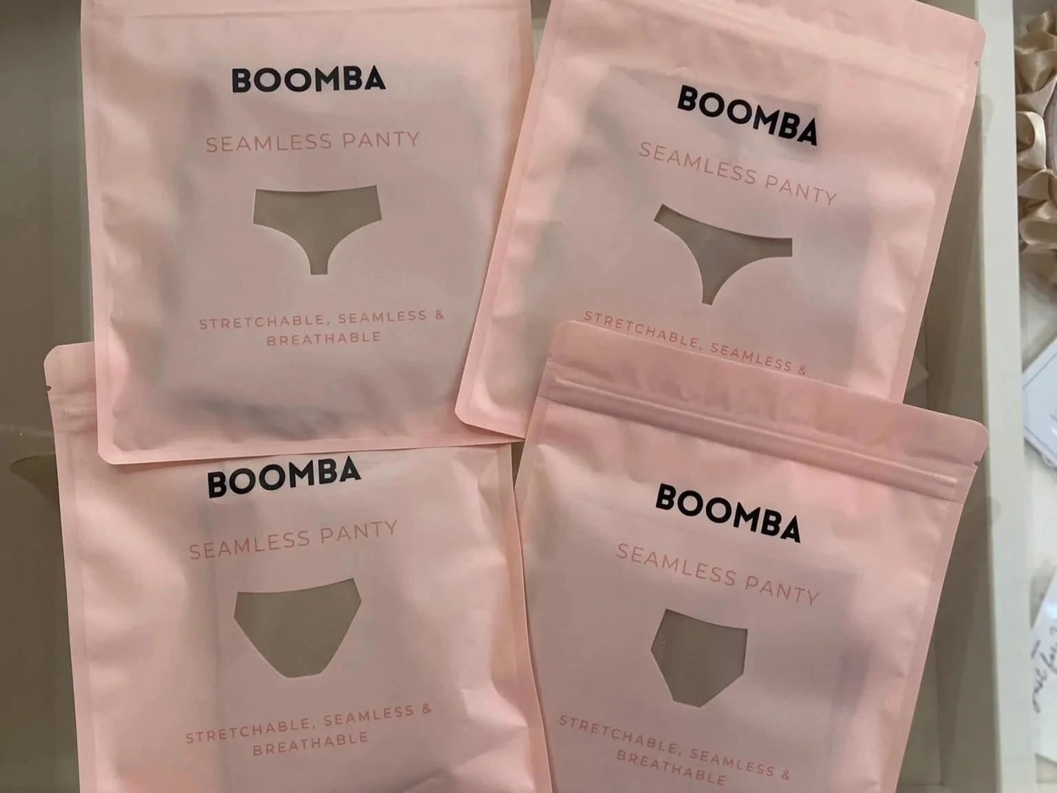 Multiple pink packages of BOOMBA Seamless Panty with a cutout window showing the panty shape. The packages are labeled with the product name and description, including features like stretchable, seamless, and breathable.