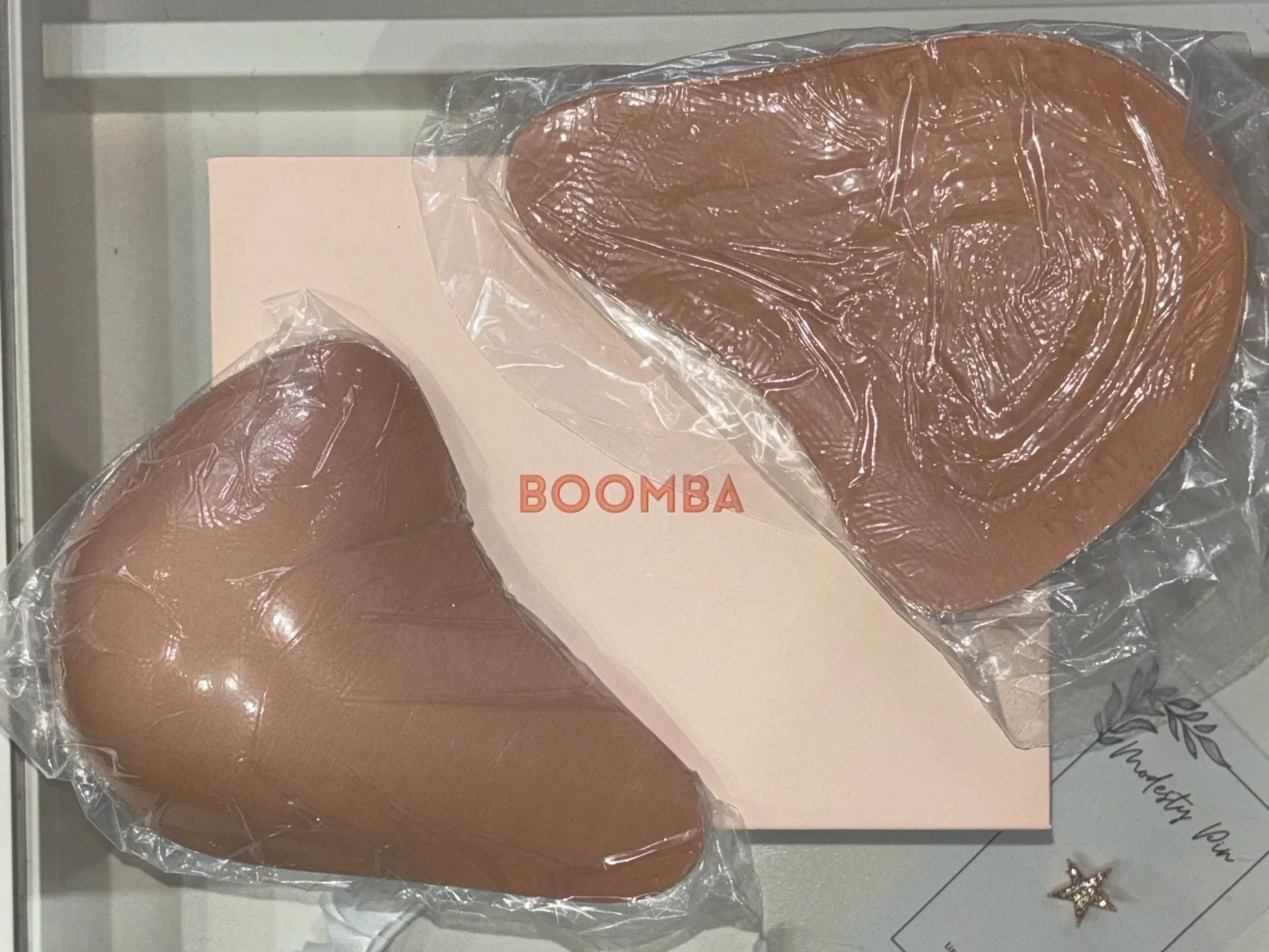 Three pieces of chocolate Bomba shaped dark chocolate on a shelf in plastic wrapping and a white box.