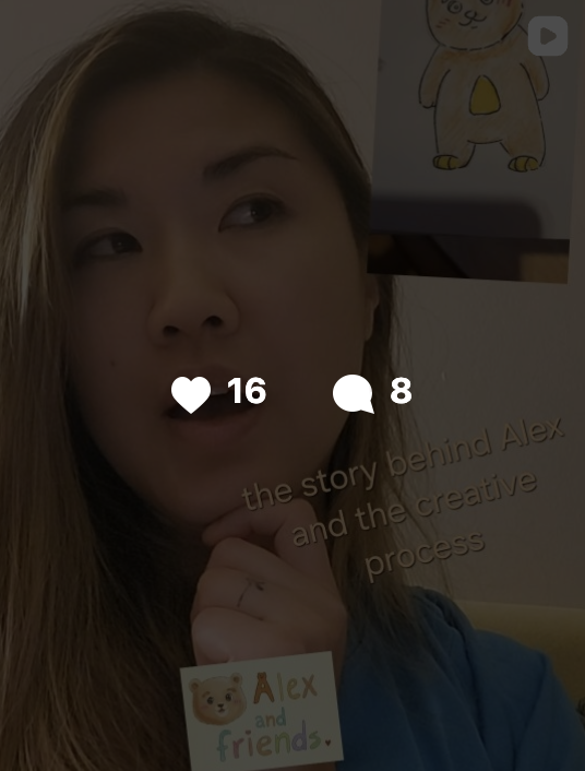 A woman with light brown hair touching her chin, in front of a wall with a drawing of a bear wearing yellow and a poster that reads 'the story behind Alex and the creative process.'