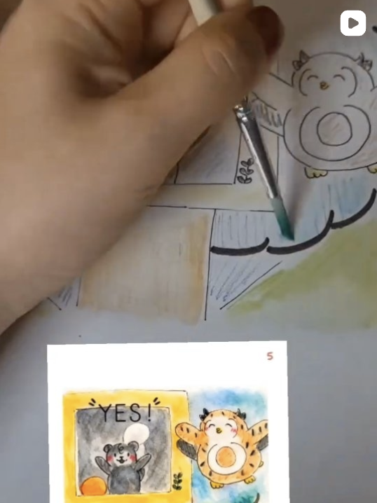 A person painting a colorful illustration of a cartoon tiger wielding a ring and a cartoon bear with a white ball on its head, with a smaller drawing of the tiger and bear on paper nearby.